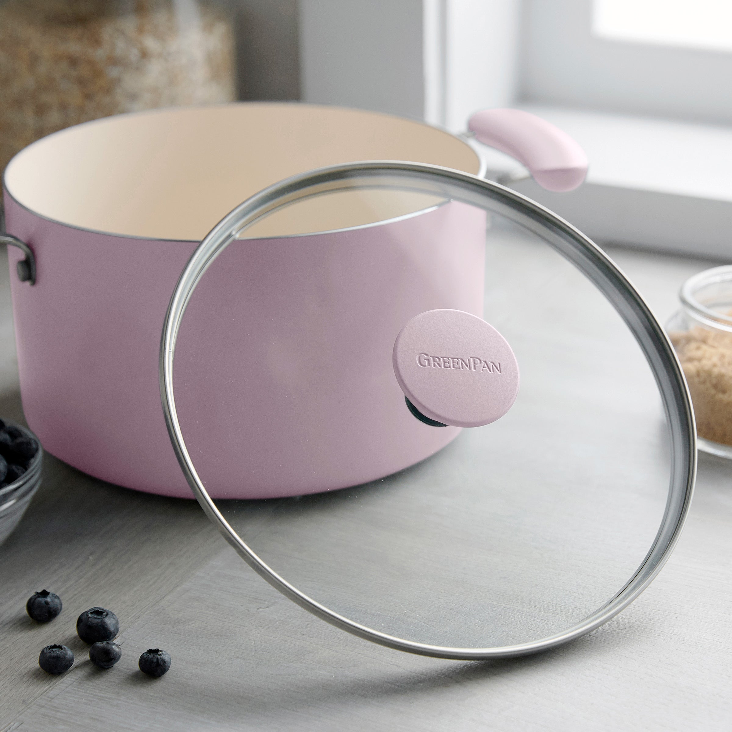 Pink 12-piece ceramic nonstick cookware set on a counter with blueberries and brown sugar nearby.