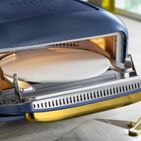 Blue pizza oven with a pizza stone inside on a light surface.