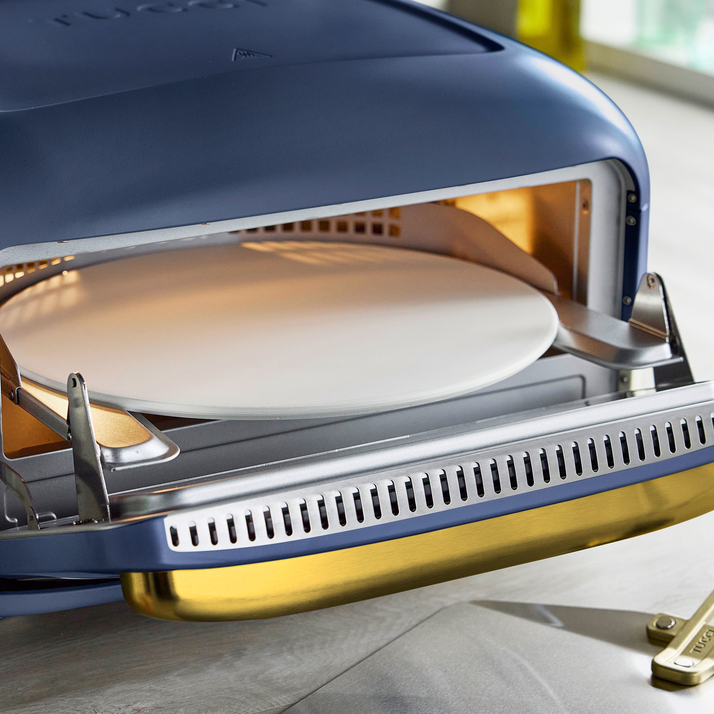 Blue pizza oven with a pizza stone inside on a light surface.