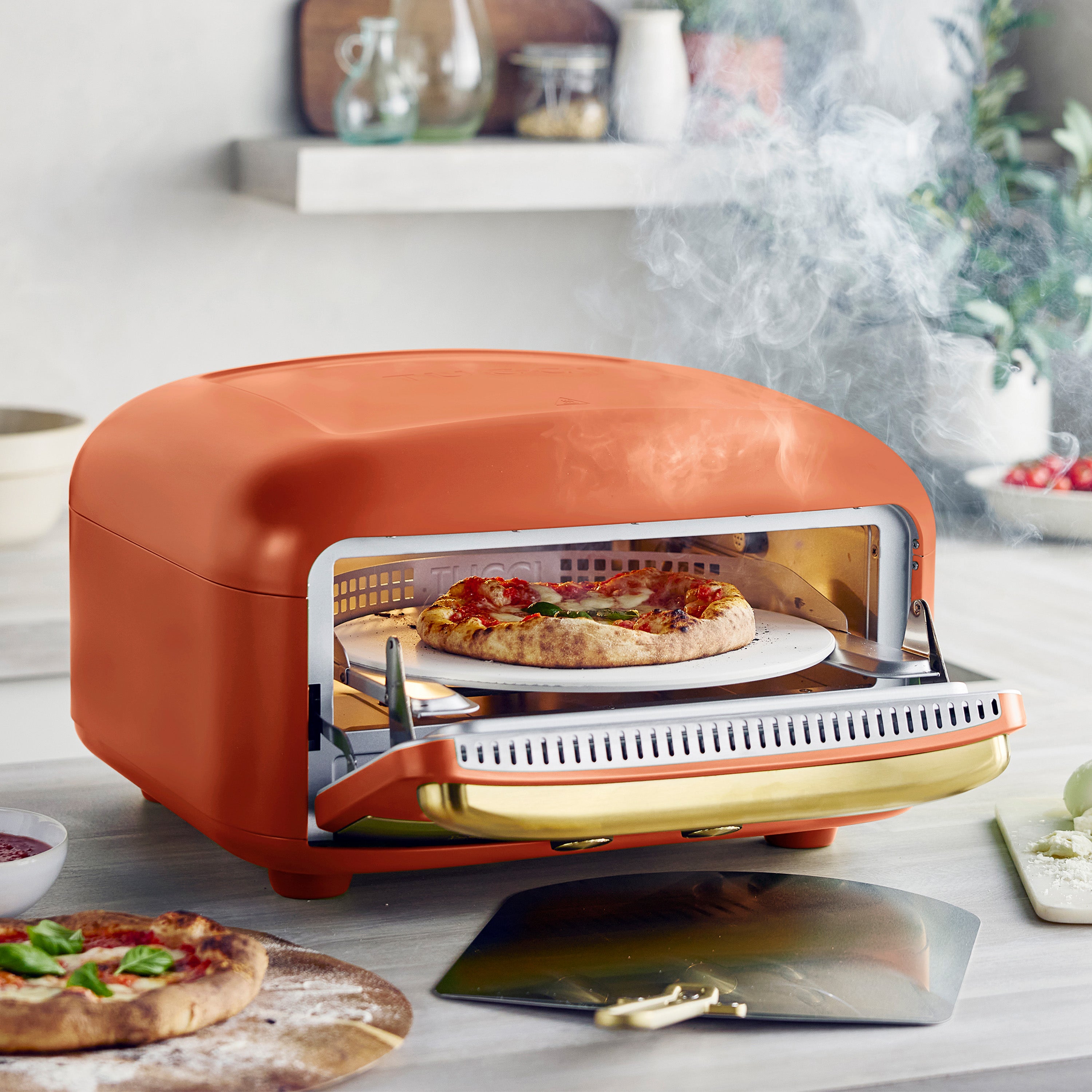 Orange pizza oven with a pizza on a pizza stone inside on a kitchen counter.