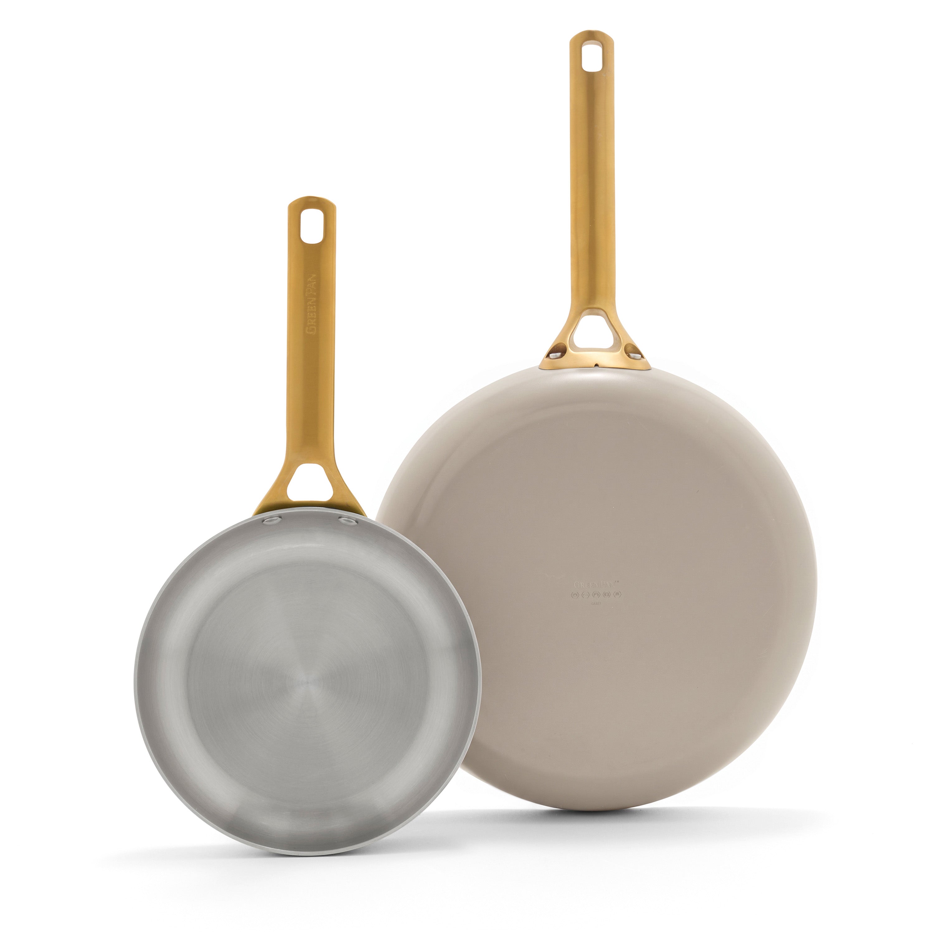 Set of two Macadamia frypans, 10″ and 12″, with gold handles, tri-ply stainless interiors, and beige bottoms.