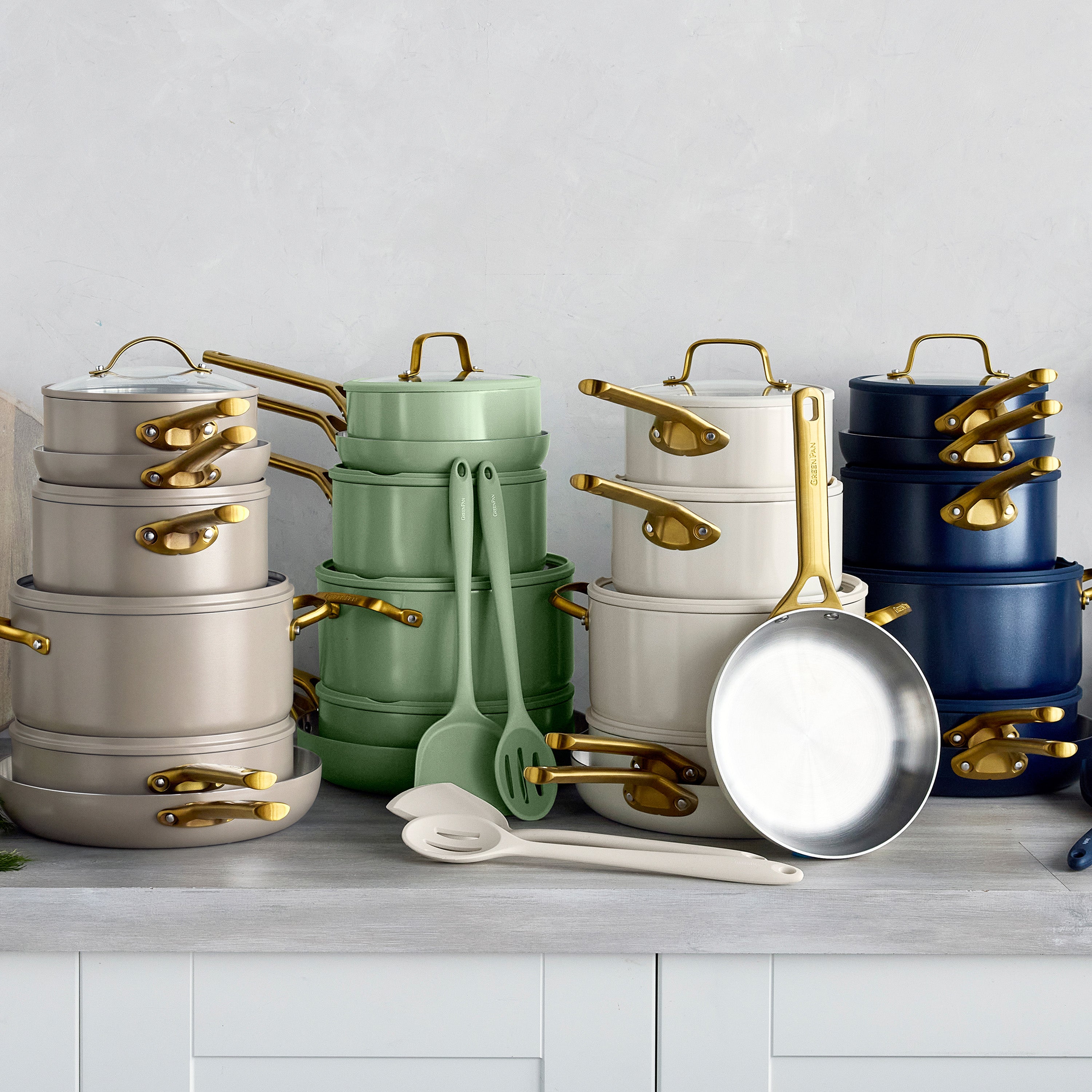 Stacked macadamia-colored stainless steel cookware sets with gold handles on a kitchen counter, 12 pieces each.