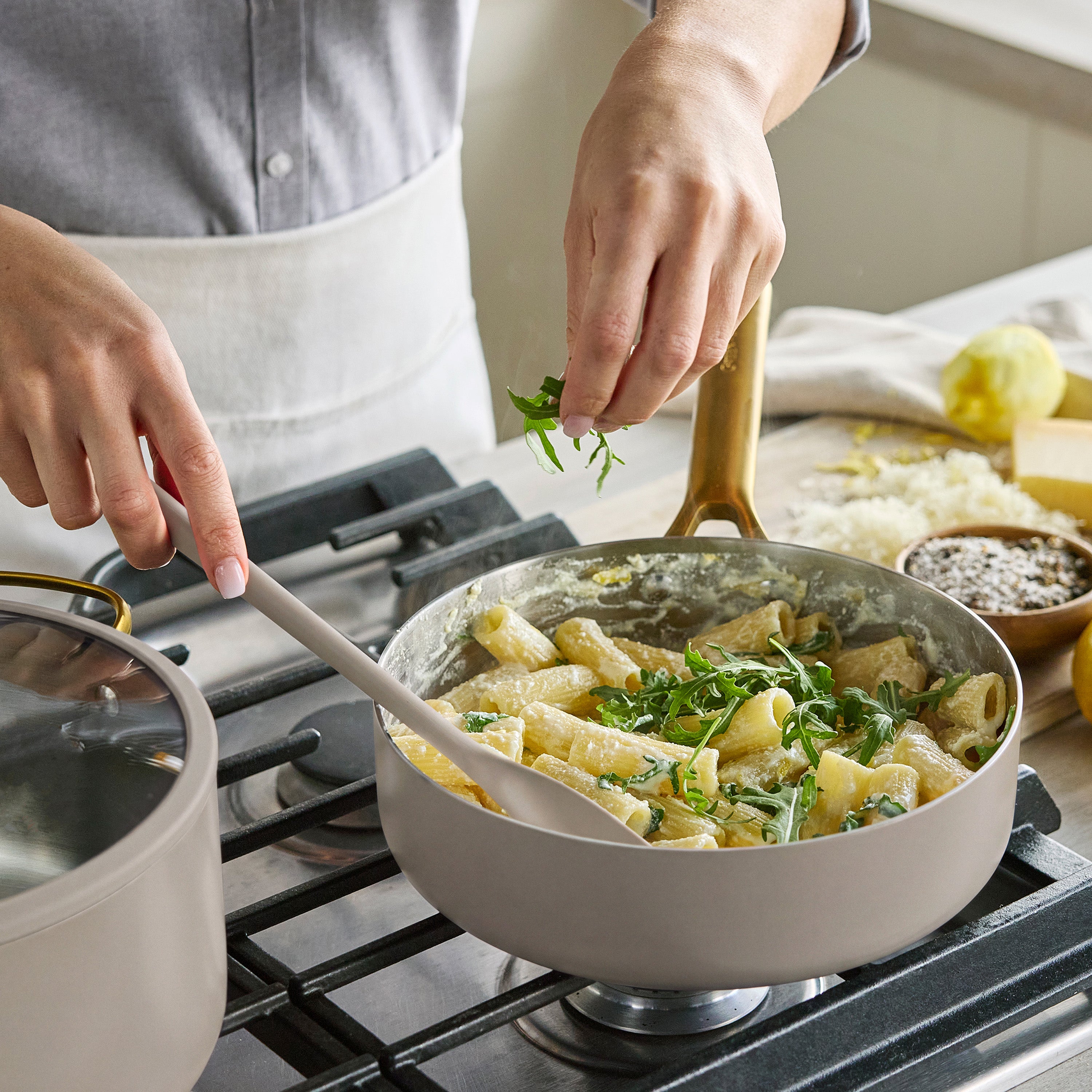 Stainless steel 12-piece cookware set on a stove, with pasta and greens being cooked in one of the pots.