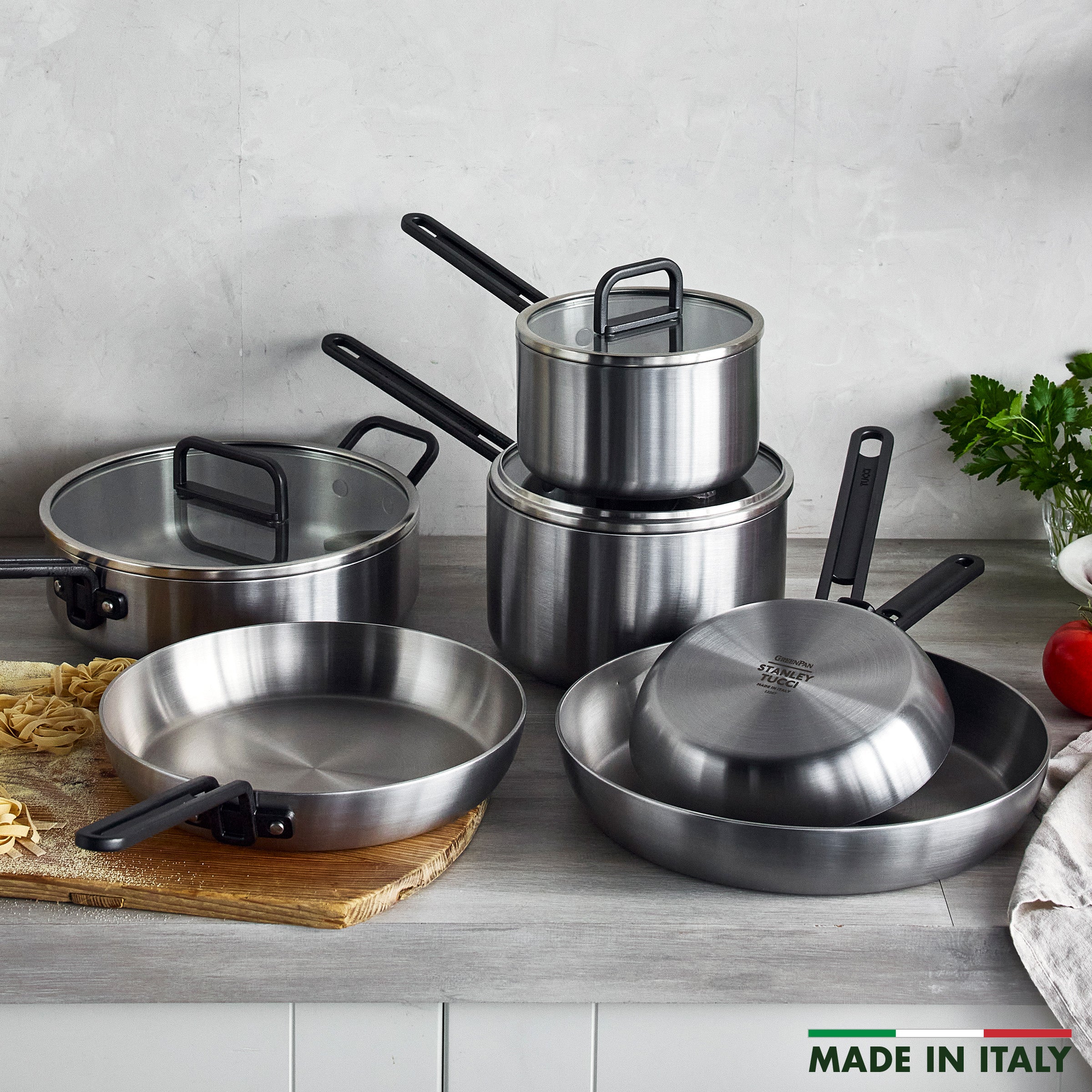 9-piece stainless steel cookware set with black handles, glass lids, herbs, and pasta visible nearby.