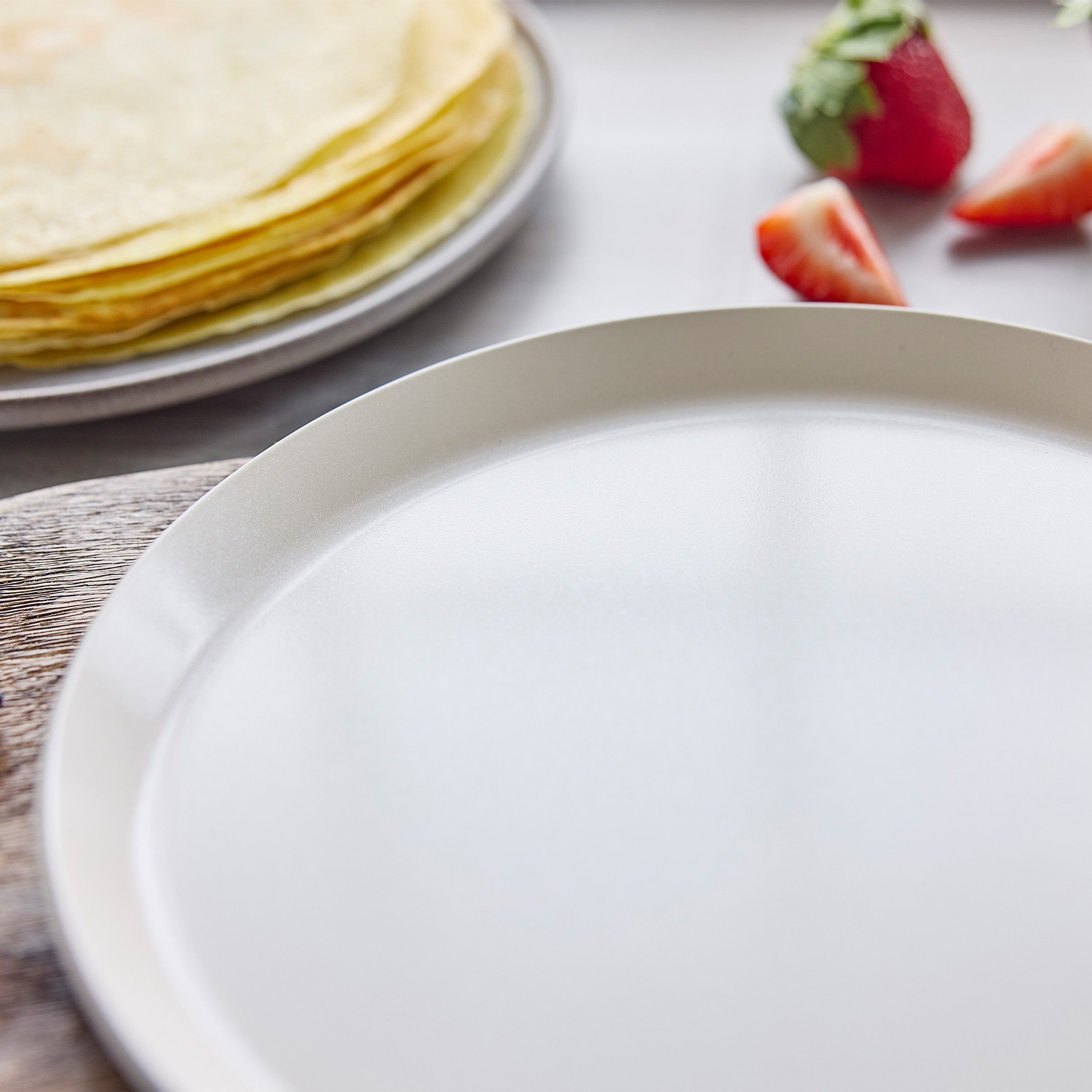 Empty plate in front, Reserve Pro Ceramic Nonstick 10″ crepe pan with crepes and strawberries in the background.