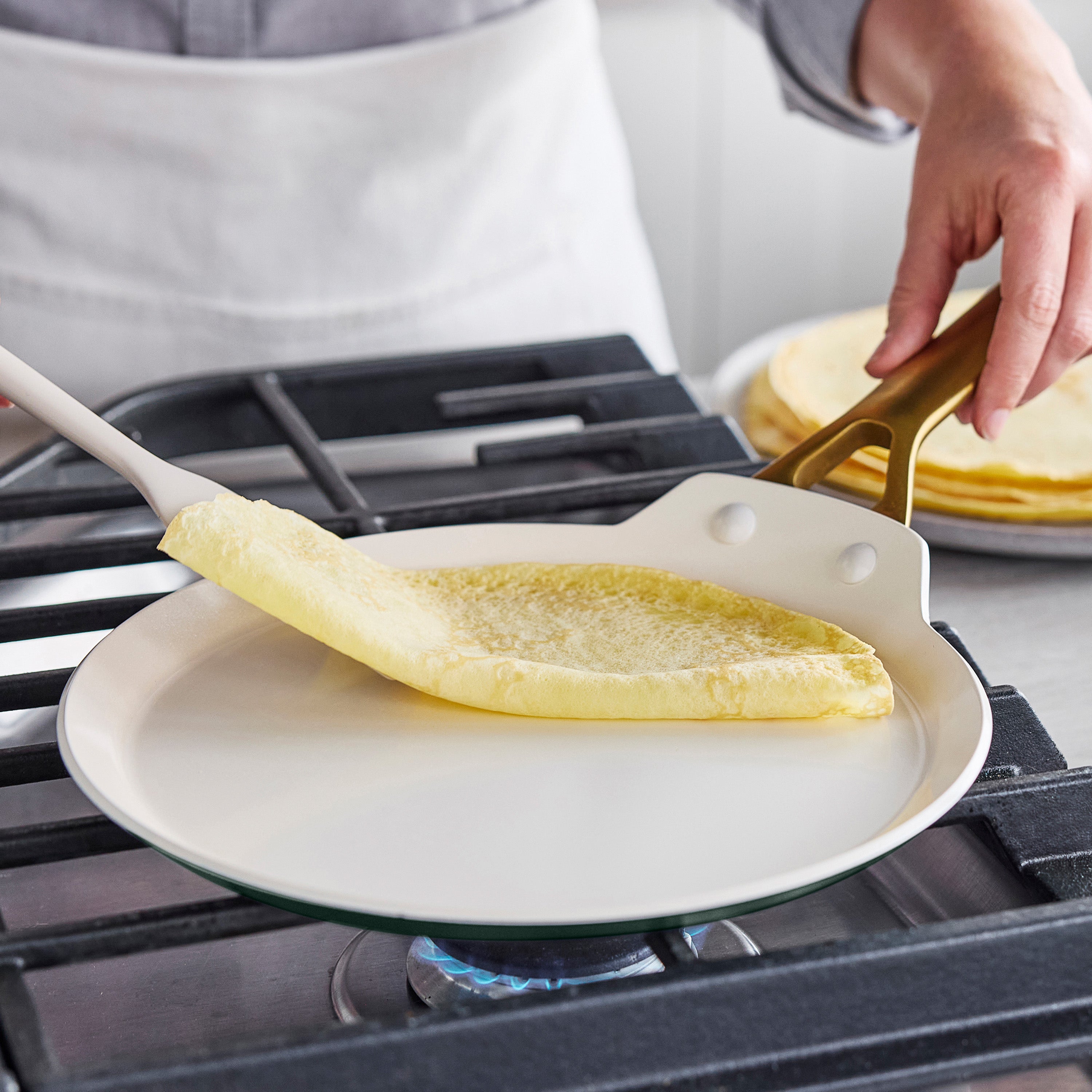 Crepe being lifted with a spatula in a gray ceramic nonstick 10″ crepe pan on a stovetop.