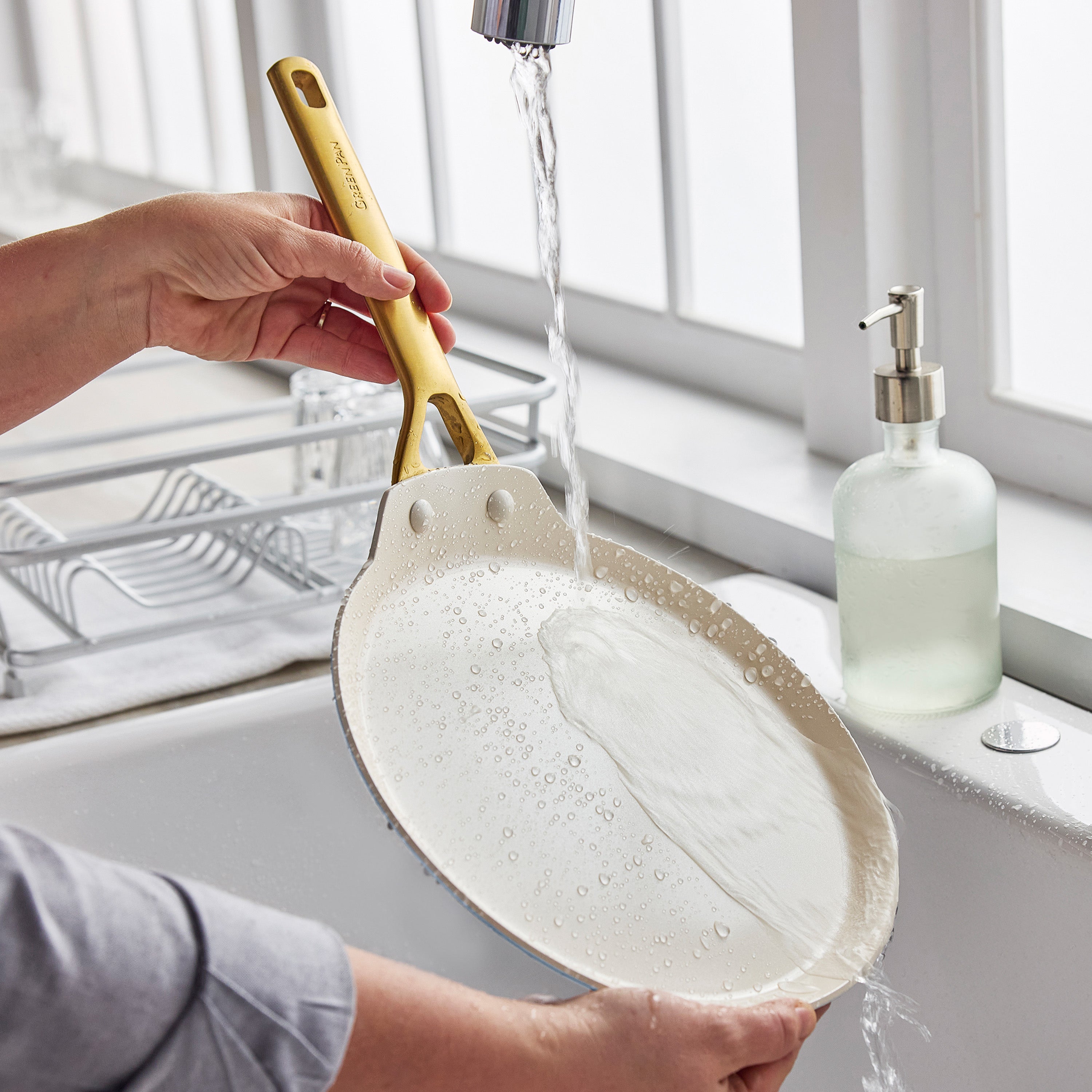 A ceramic nonstick 10″ crepe pan being washed under running water at a kitchen sink.