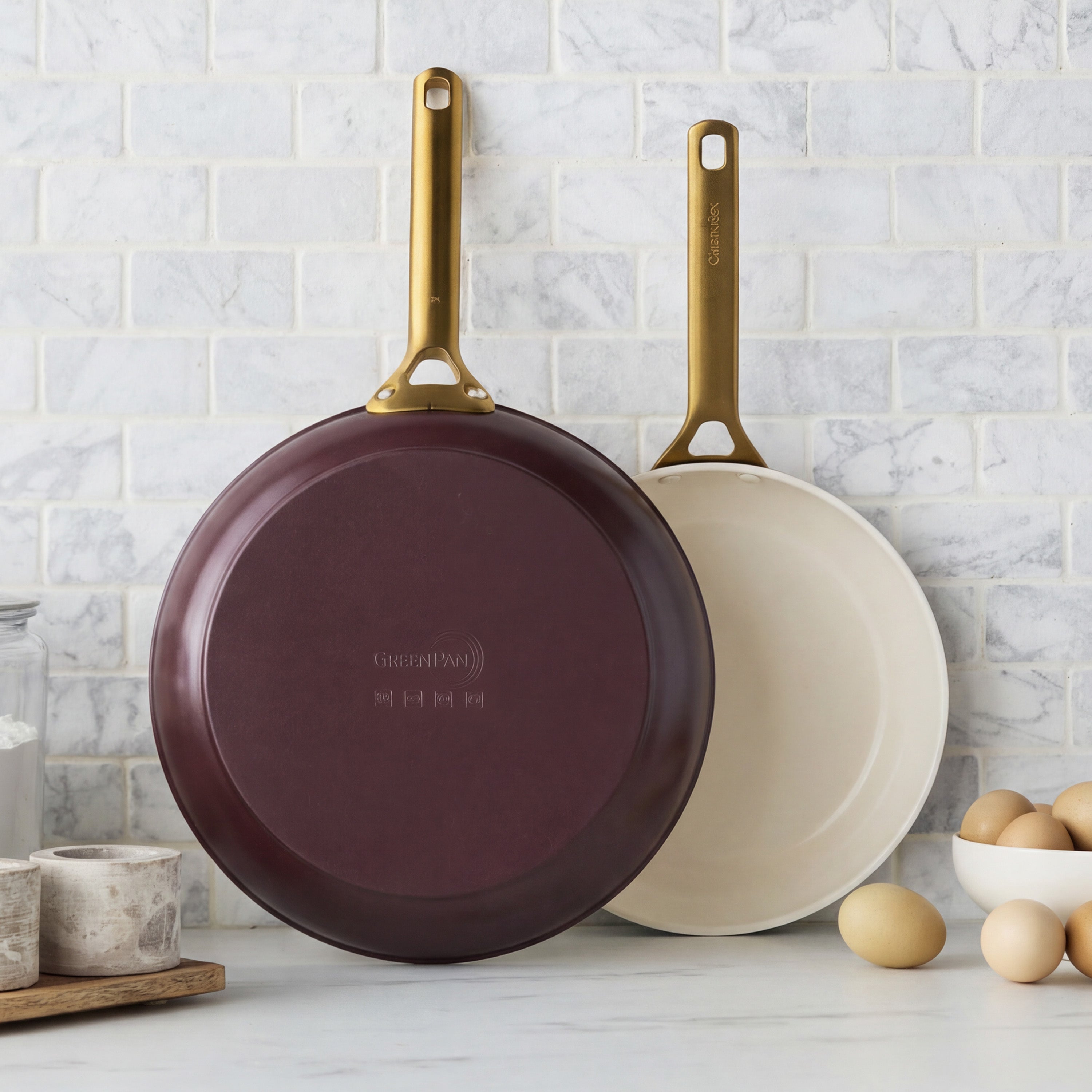 Two maroon ceramic nonstick frypans with cream interiors next to fresh eggs; 10-inch and 12-inch set.