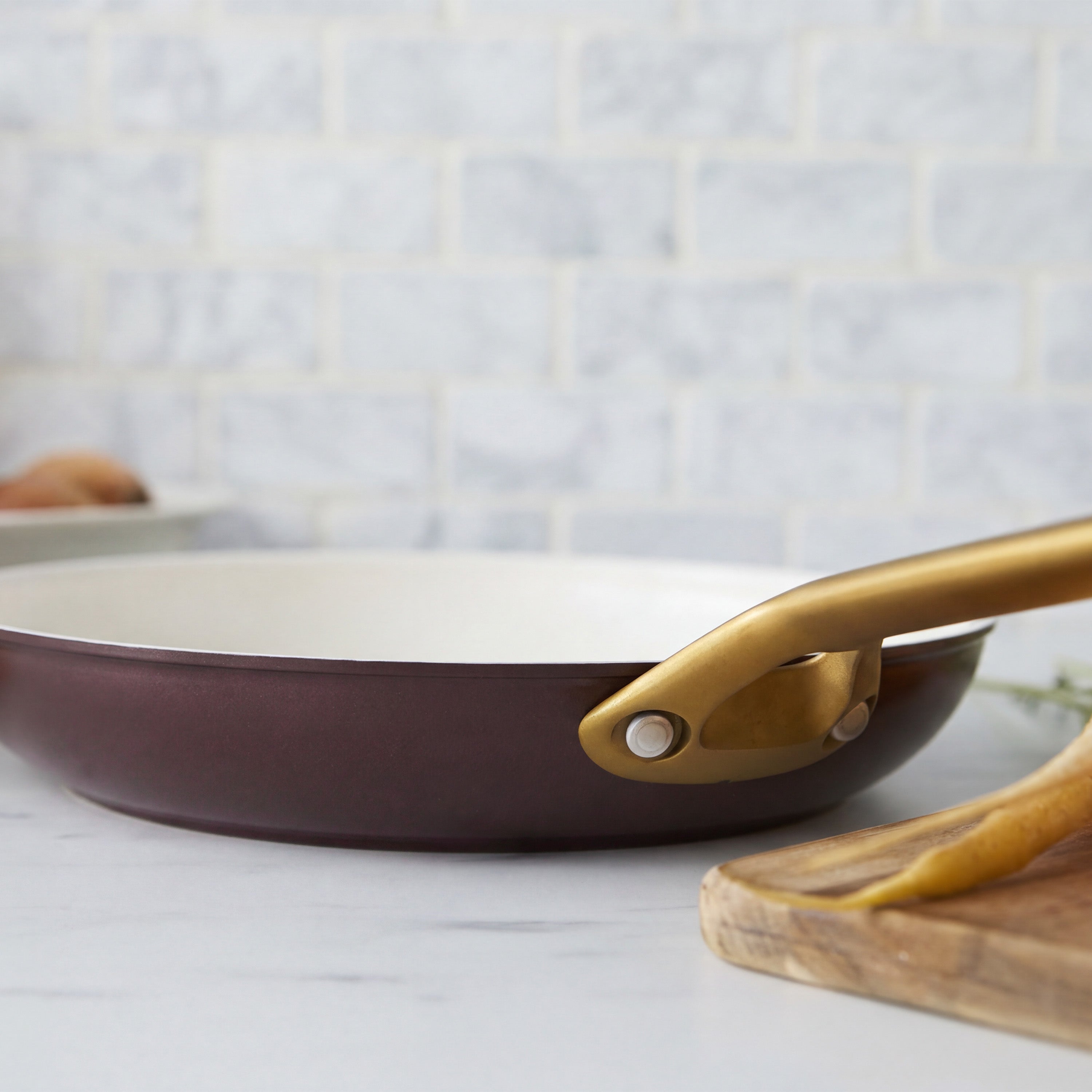 Two Bordeaux ceramic nonstick frypans, 10″ and 12″, on a white counter next to a wooden cutting board.