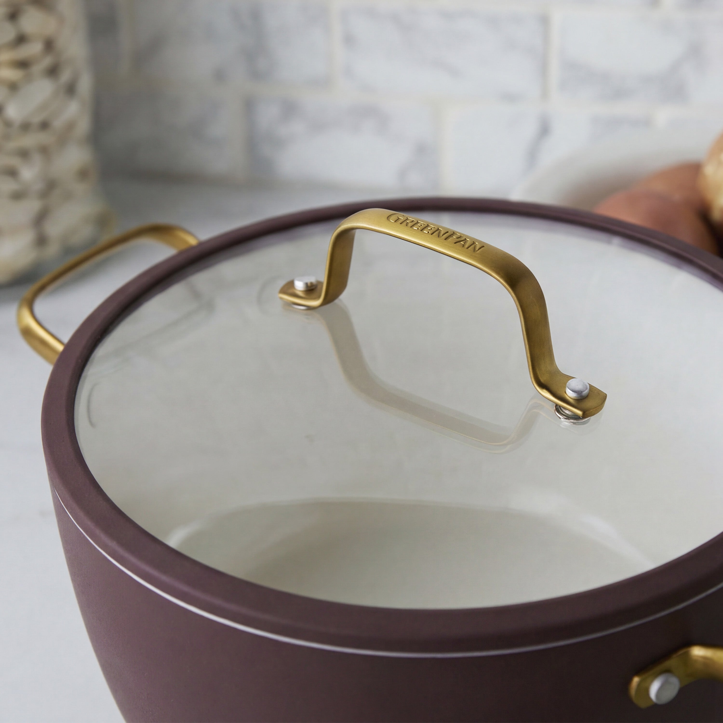 Bordeaux ceramic nonstick cookware set with gold handles and glass lid, stacked on a counter, 10 pieces visible.
