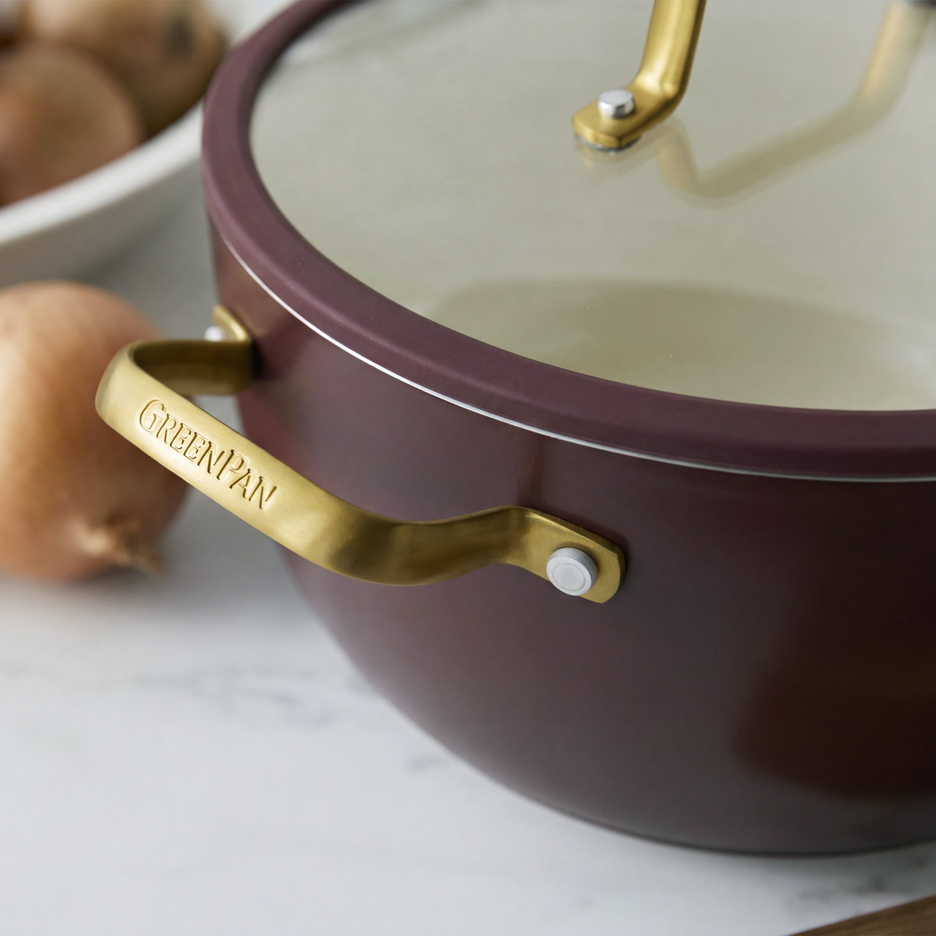 Bordeaux ceramic nonstick 10-piece cookware set with gold handles, arranged on marble next to onions.