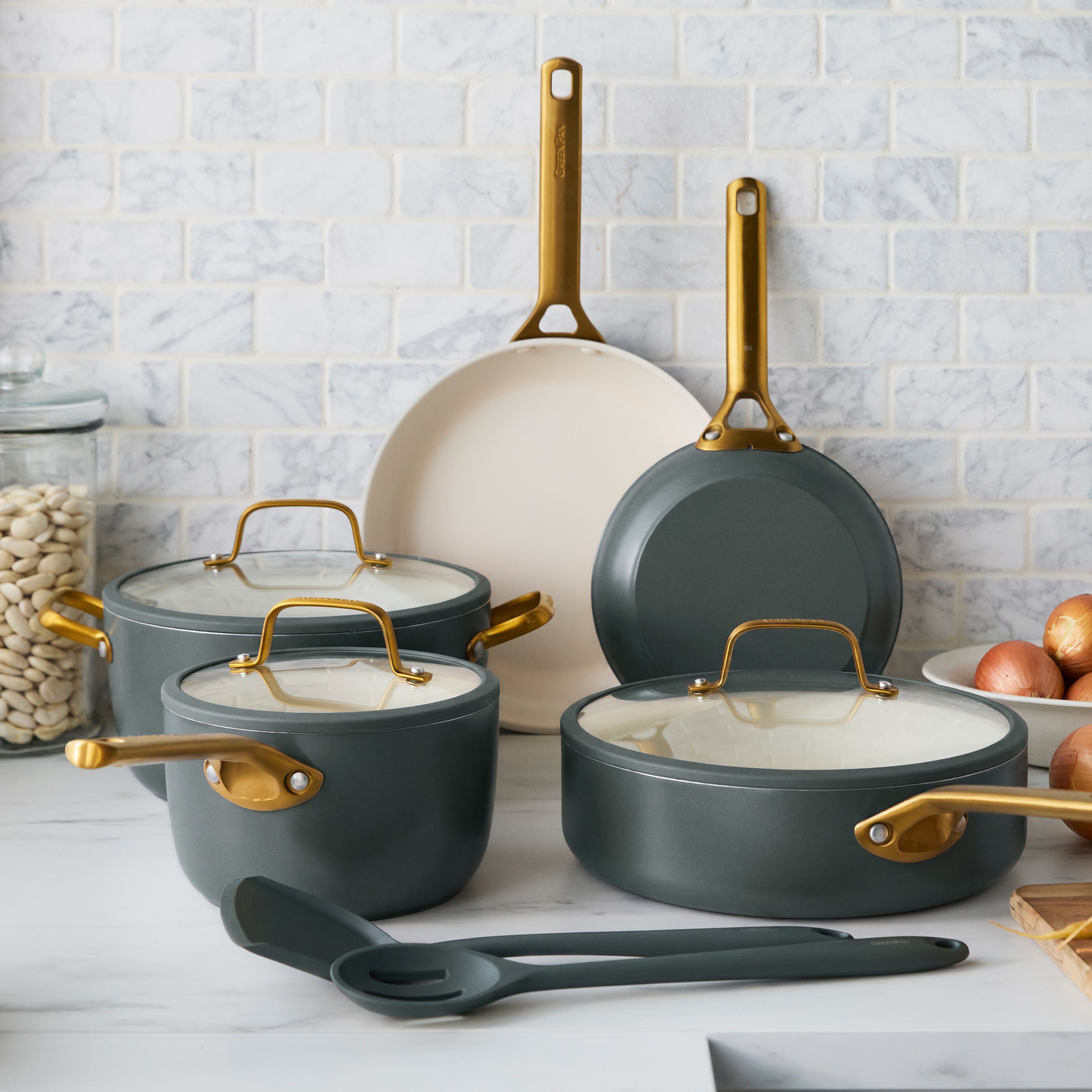 Stacked green ceramic cookware set with gold handles on a kitchen counter, next to onions and beans. Ten pieces visible.