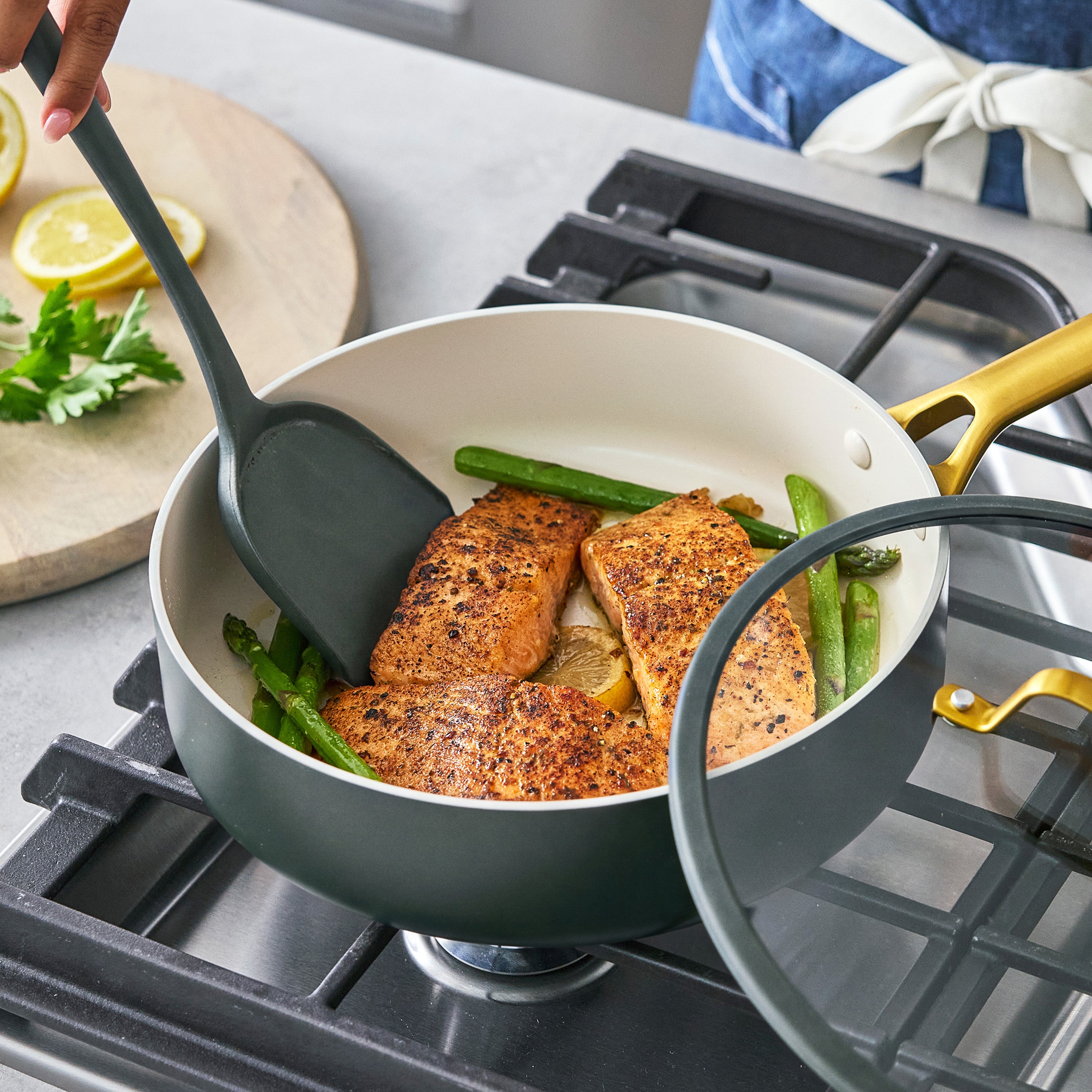 Salmon and asparagus cook in a gray ceramic nonstick pan, with lemon wedges and herbs on the side.