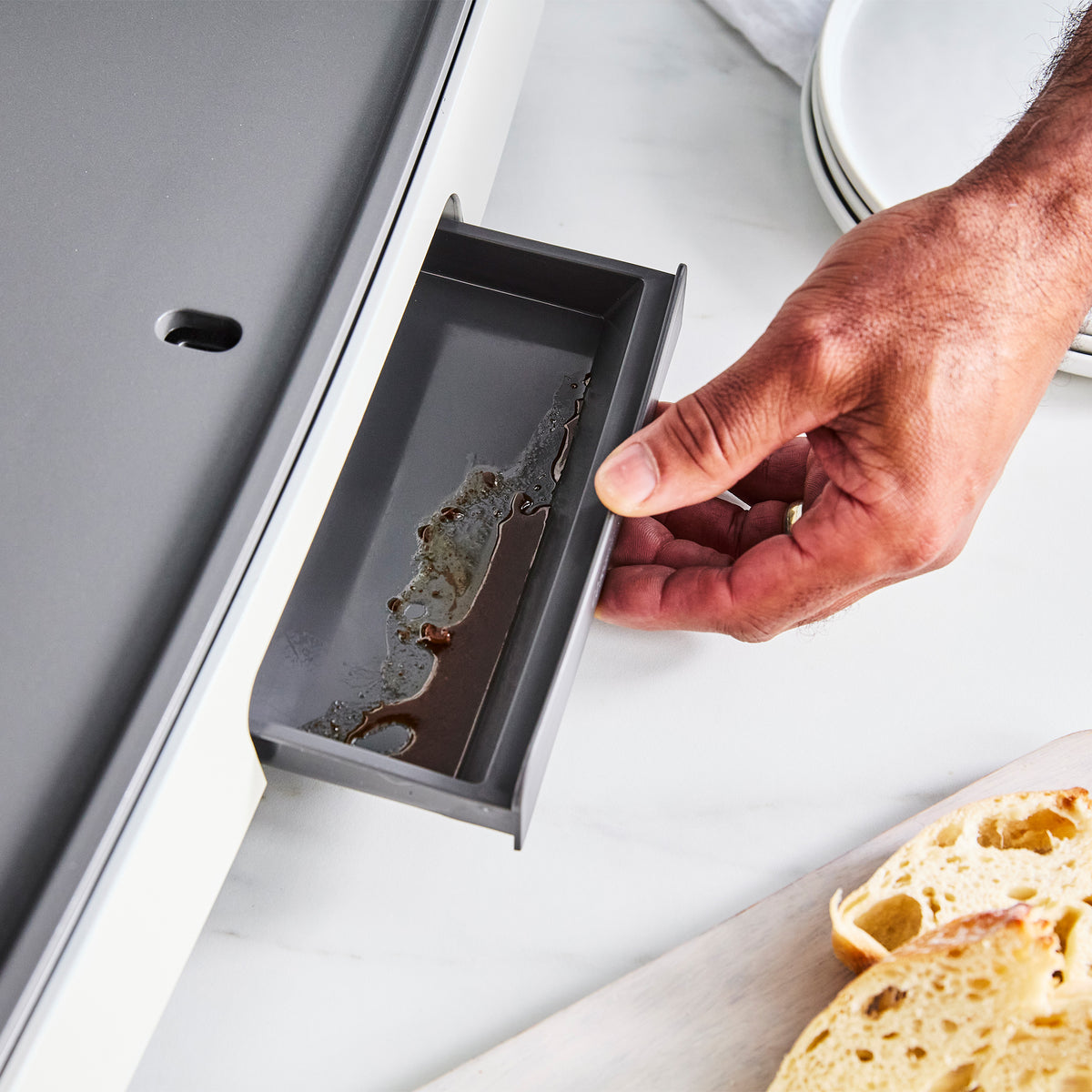 A hand sliding the drip tray out of a Cloud Cream Ultimate Countertop Griddle.