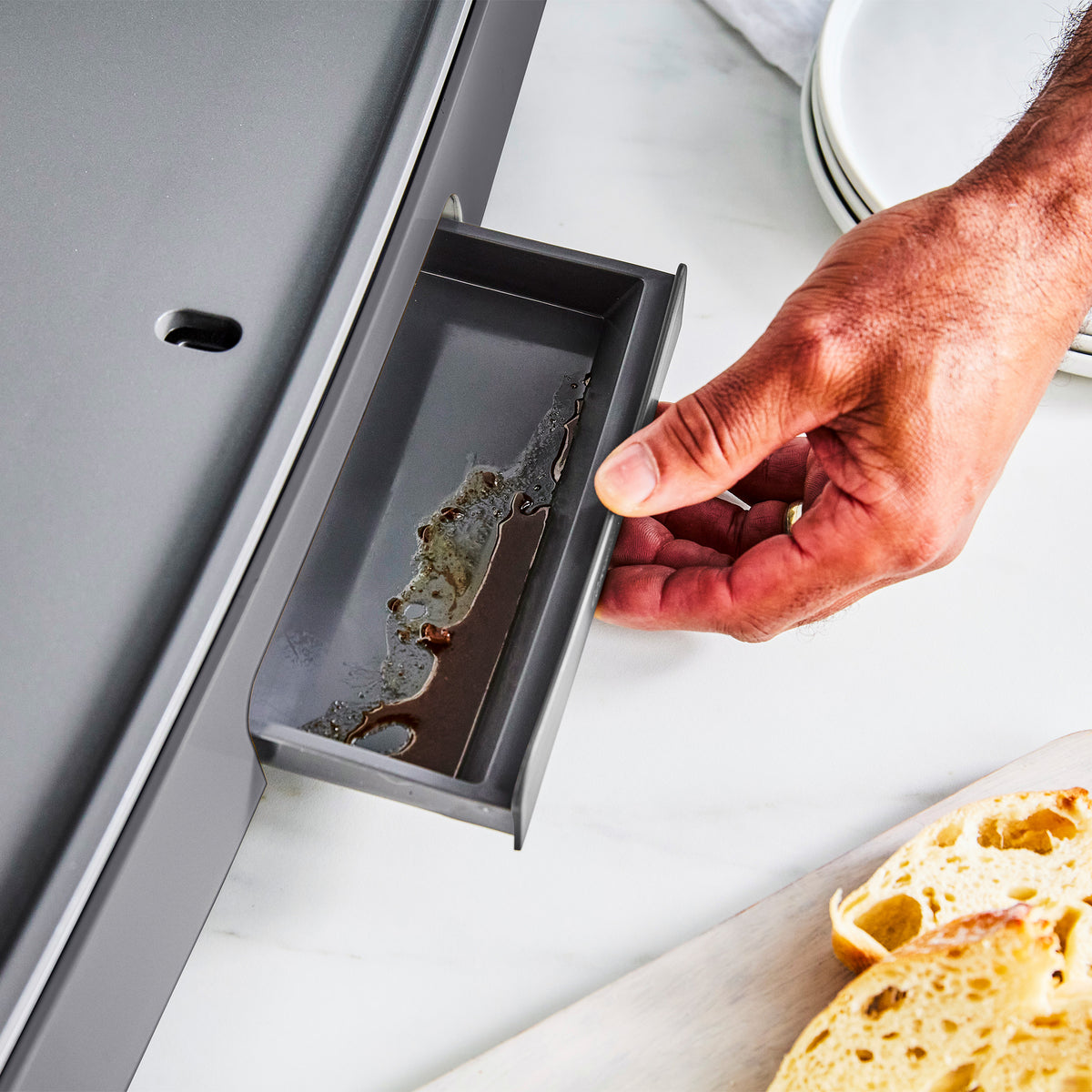 A hand pulling the drip tray out from the Graphite Ultimate Countertop Griddle.
