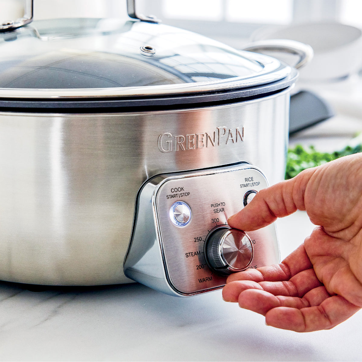 Hand adjusting temperature dial on stainless steel electric wok with black handles, 6-quart size visible.