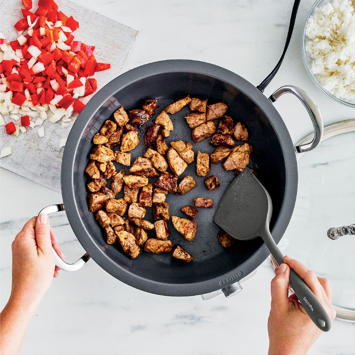 Chef cooks chicken, vegetables, and rice in a black Premiere 6-quart electric wok on a marble countertop.