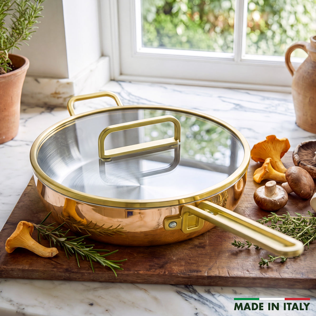 Copper Stanley Tucci pan with lid on wood board, surrounded by herbs, mushrooms, and ‘MADE IN ITALY’ text.