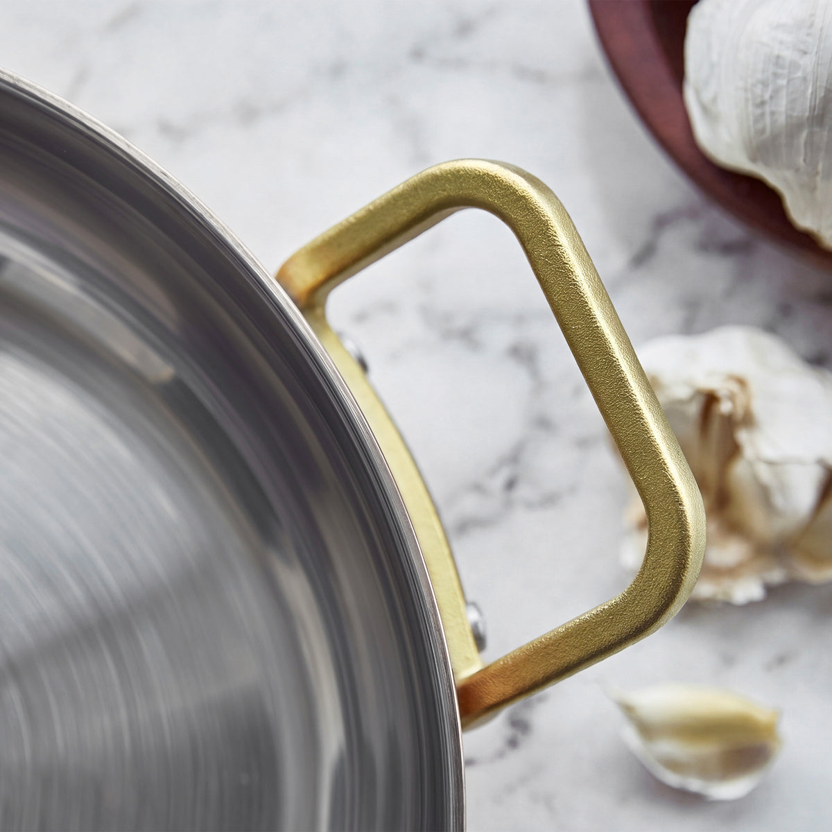 Copper 4.5-quart saucepan with gold handle on marble, next to garlic cloves and a brown plate.