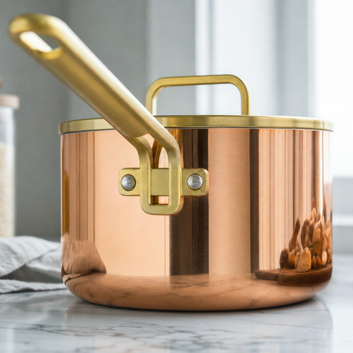Copper 4-quart saucepan with lid on a marble countertop by a window.