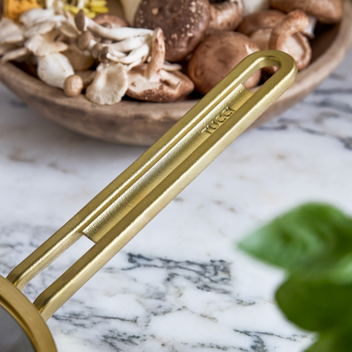 Copper saucepan with lid on marble surface, mushrooms in a wooden bowl nearby.