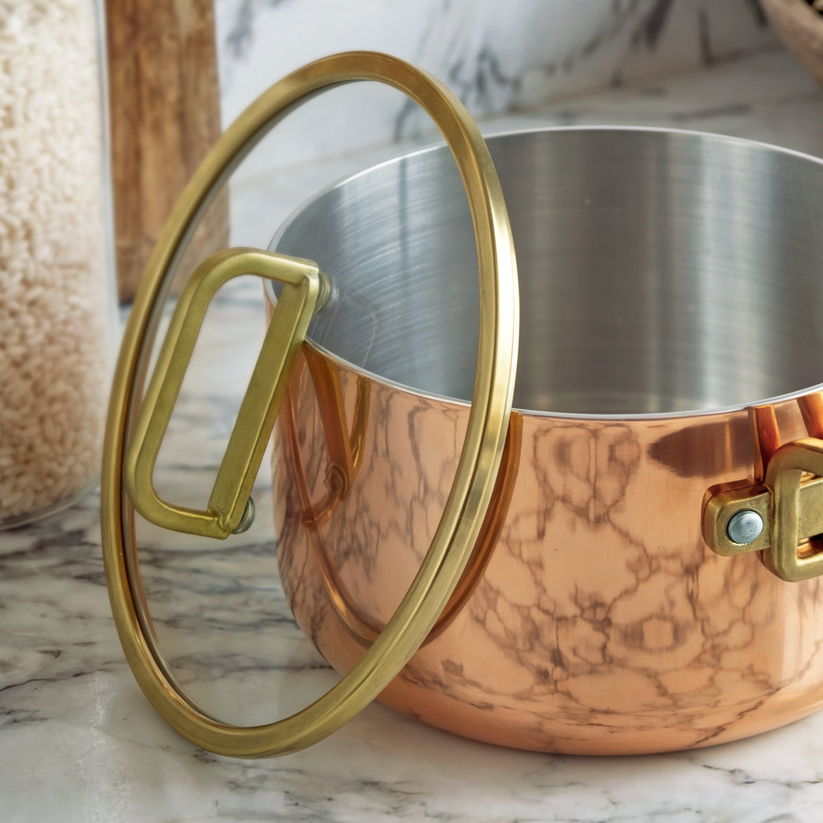 Copper 4-quart saucepan with lid open on a marble countertop next to a glass jar of rice.