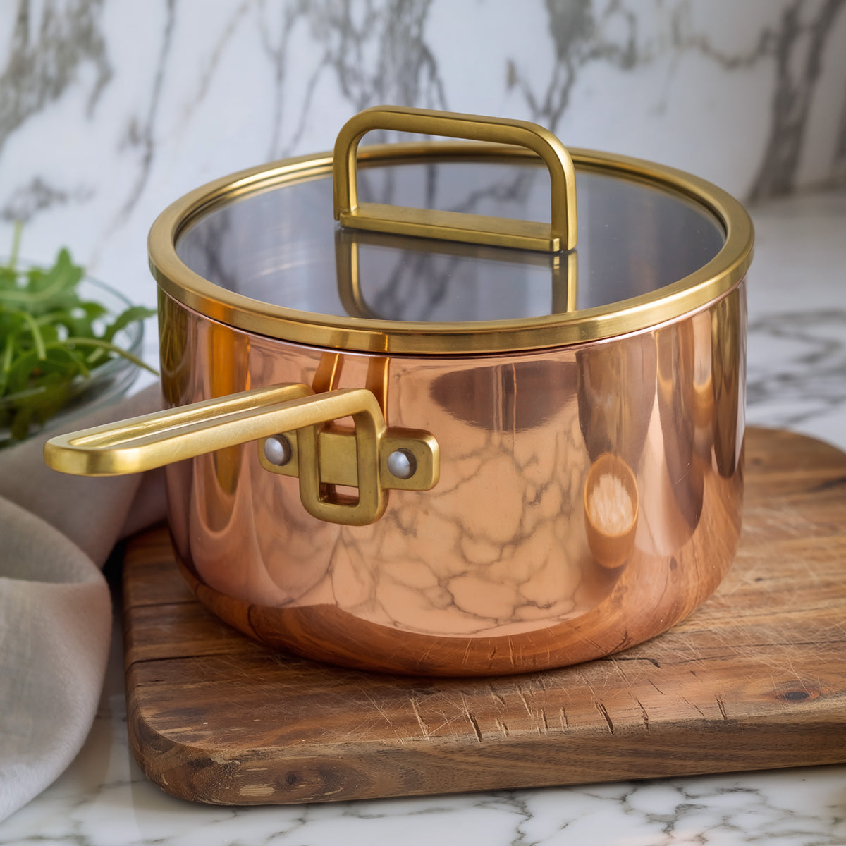 Copper saucepan with lid on a wooden board atop a marble counter.