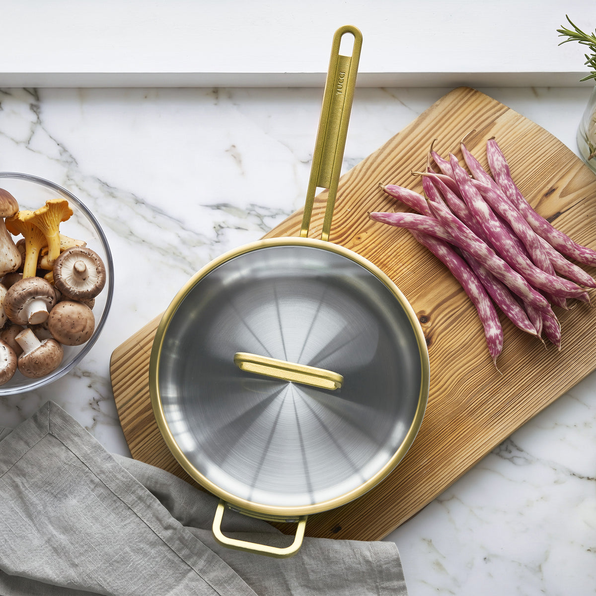 Copper 4-quart sauté pan with lid on marble counter, next to a cutting board with green beans and mushrooms.