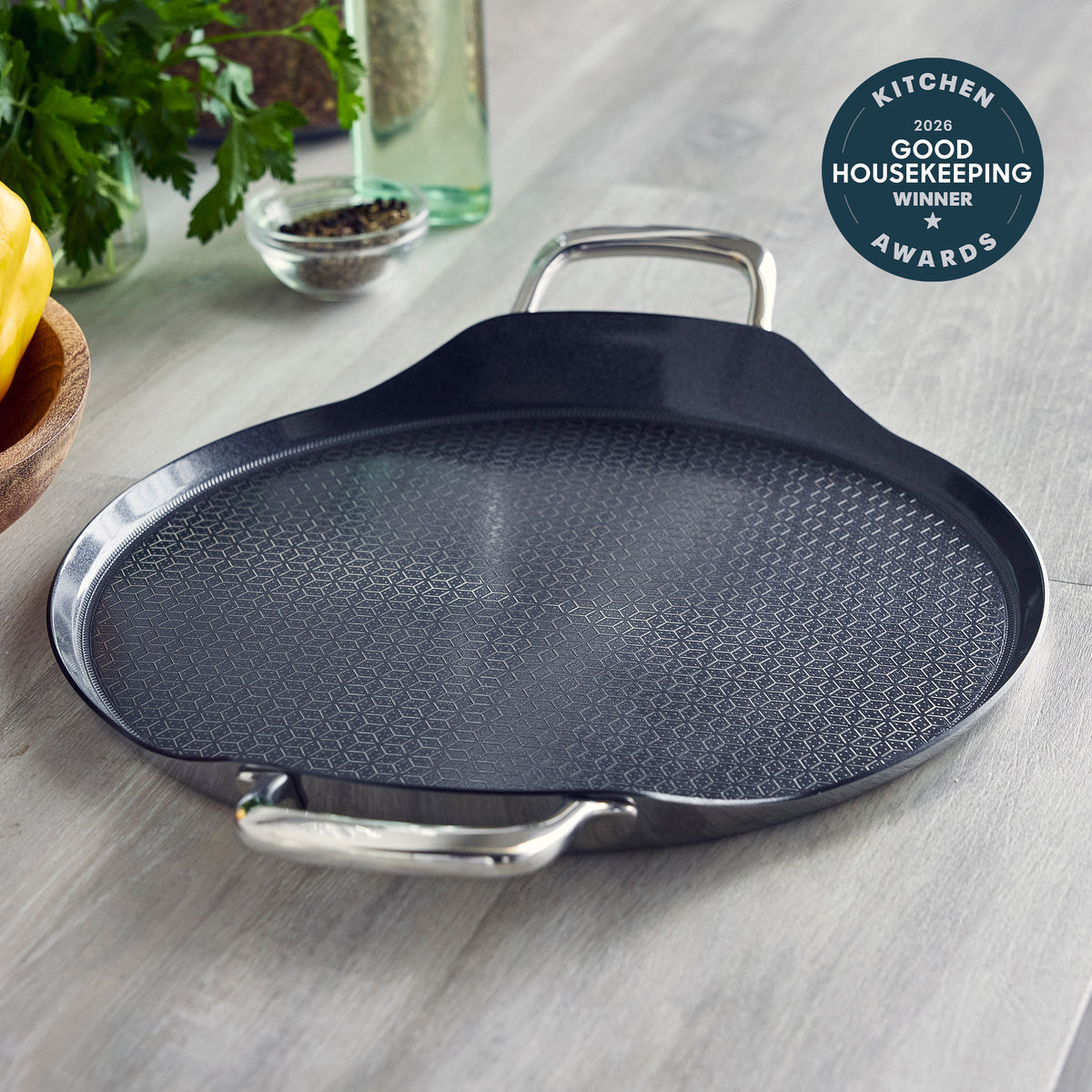 Spectra Thermobond 13-inch round ceramic griddle with a textured interior and two stainless steel handles.