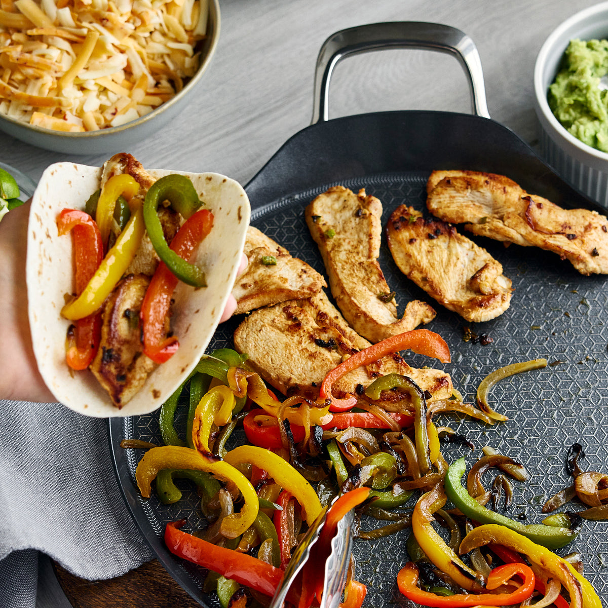 Spectra Thermobond 13″ round ceramic griddle cooking chicken, peppers, and onions, with a hand filling a tortilla.