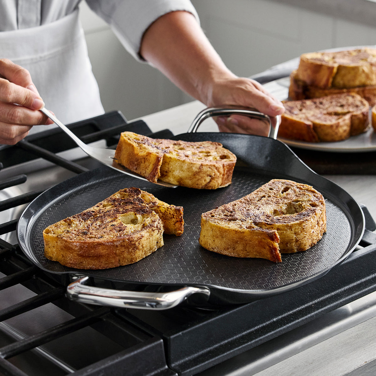 Spatula lifting French toast from a 13″ round Spectra Thermobond ceramic nonstick griddle on a stovetop.