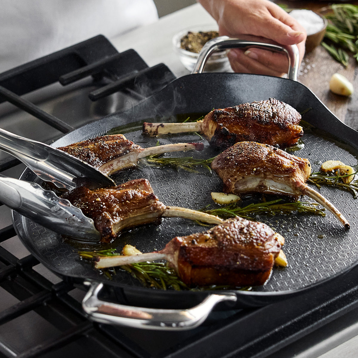 Lamb chops cooking with rosemary and garlic on a Spectra Thermobond 13″ round ceramic nonstick griddle.