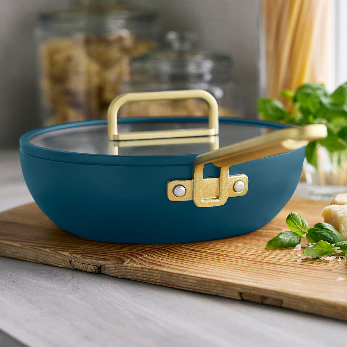 Stanley Tucci 3.25-quart ceramic nonstick Piccolo pan in Venetian Teal with a gold-tone handle and glass lid on a wooden cutting board.