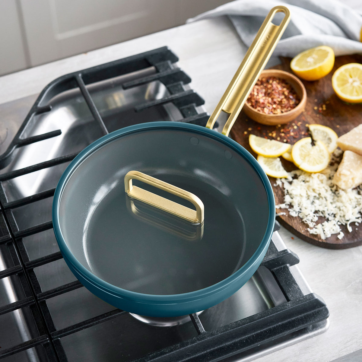 Stanley Tucci 3.25-quart ceramic nonstick Piccolo pan in Venetian teal on a stovetop with lemons and grated cheese on a cutting board.