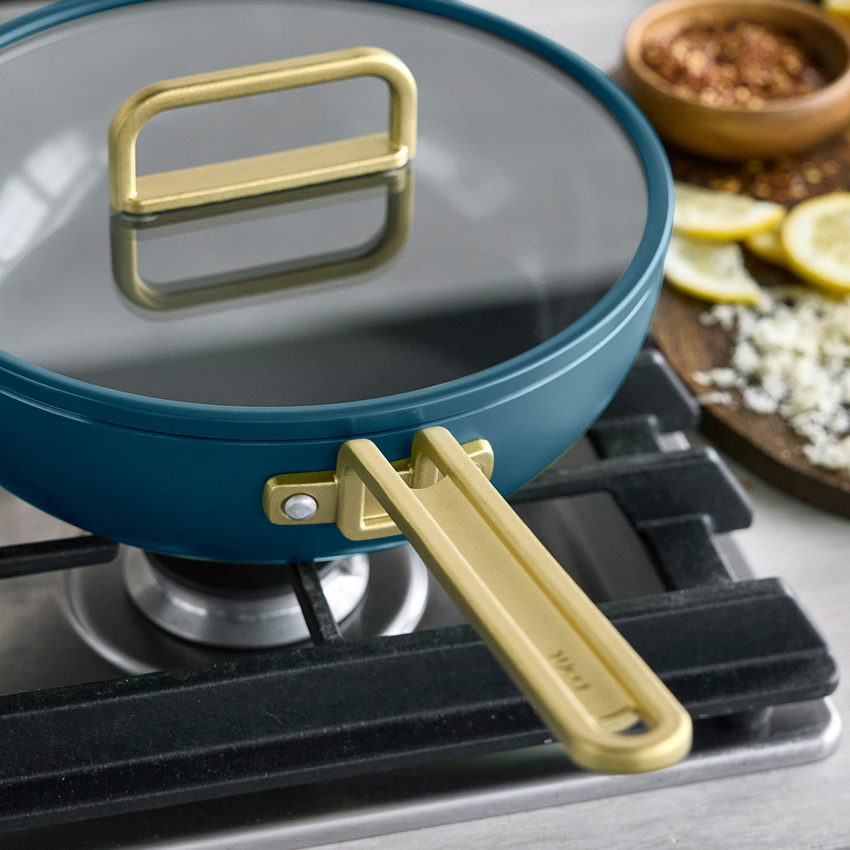 Stanley Tucci 3.25-quart ceramic nonstick Piccolo pan in Venetian Teal with a gold-tone handle and glass lid on a stovetop.