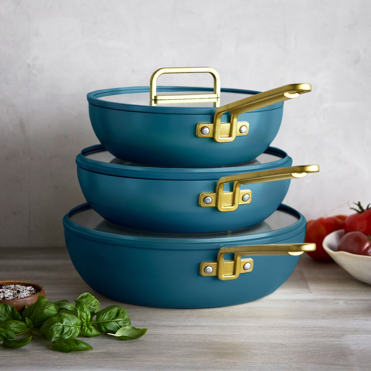 Three stacked Venetian Teal Stanley Tucci 3.25qt ceramic nonstick piccolo pans with gold handles and glass lids. Made in Italy.