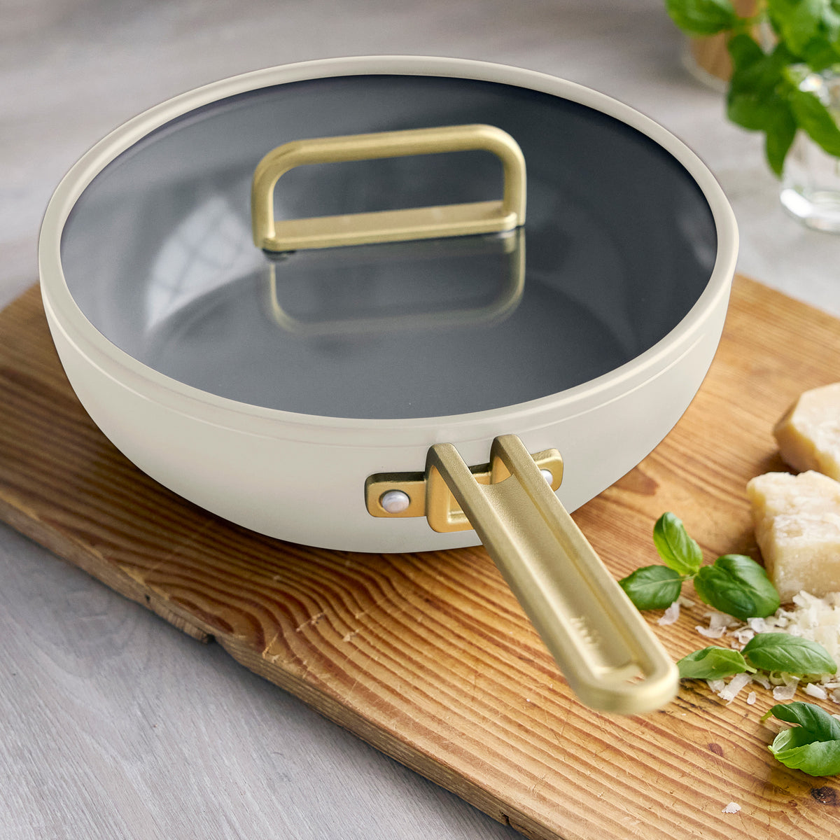 Stanley Tucci 3.25-quart ceramic nonstick Piccolo pan in Carrara white with a gold handle and lid on a wooden cutting board.