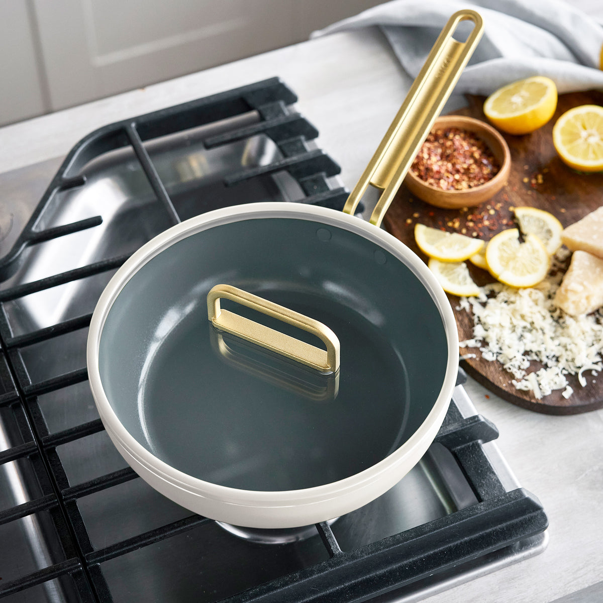 Stanley Tucci 3.25-quart white ceramic skillet with a gray interior sitting on a stove burner.