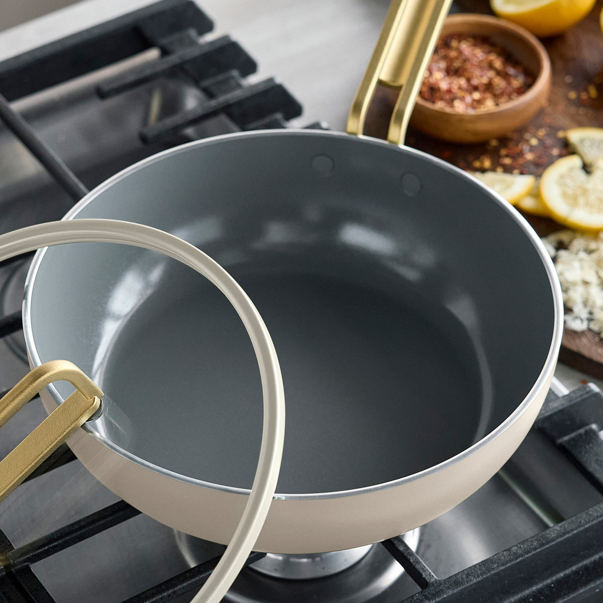 Carrara White Stanley Tucci™ 3.25-quart ceramic nonstick Piccolo pan with a gold-tone handle and glass lid on a stovetop.