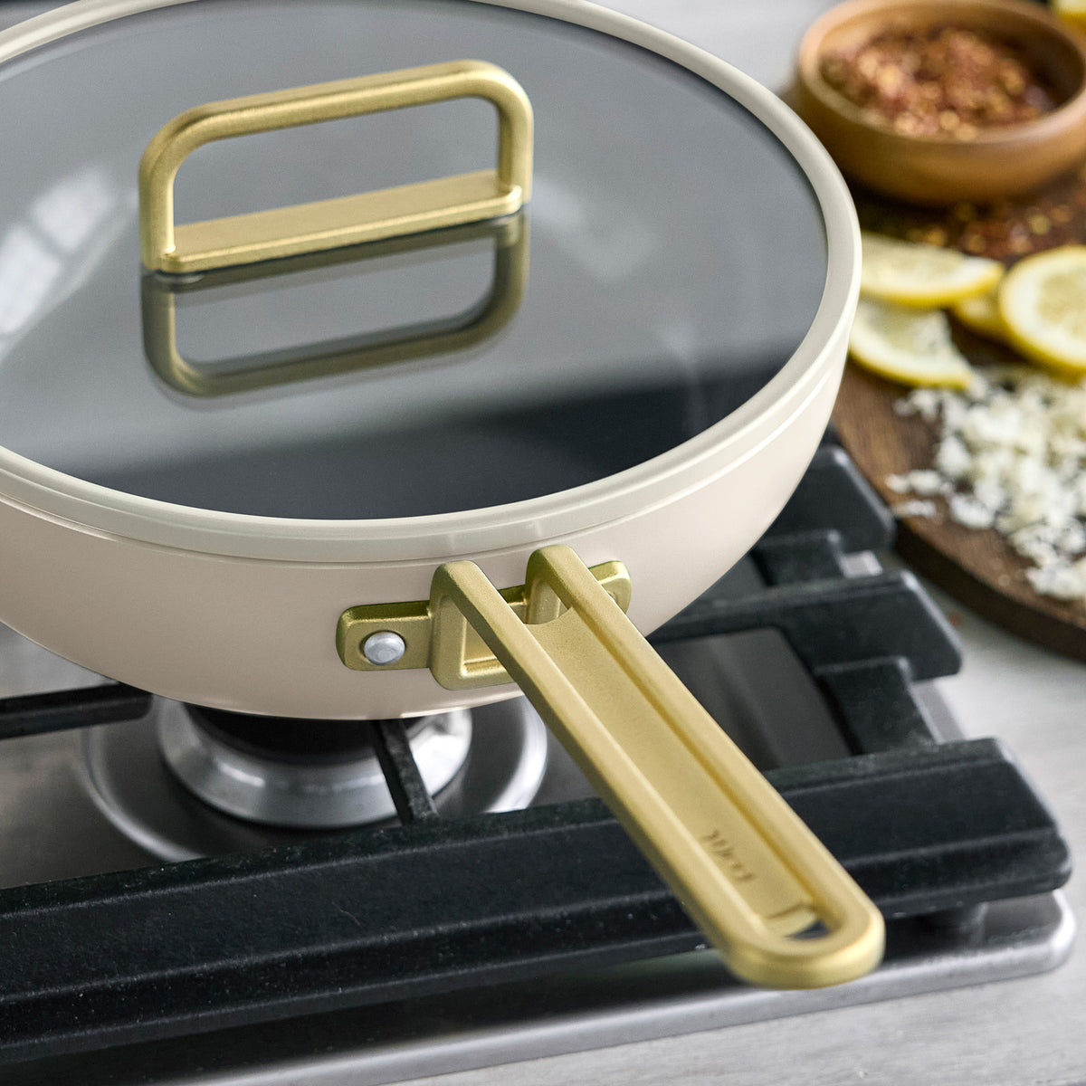 Stanley Tucci 3.25-quart ceramic nonstick Piccolo pan in Carrara White with matching lid and gold-tone handles on a stovetop.