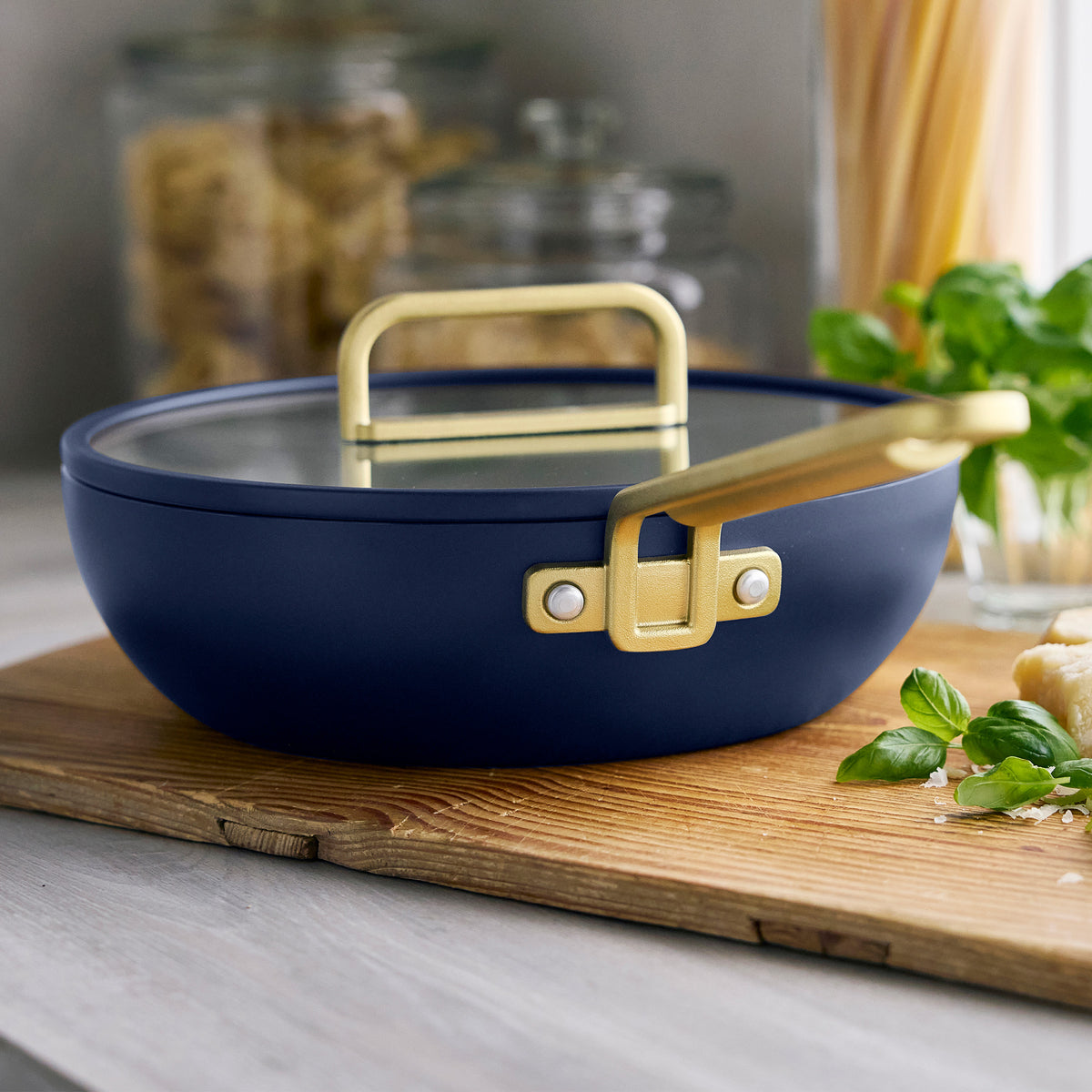 Marino blue Stanley Tucci 3.25-quart ceramic nonstick piccolo pan with a glass lid and gold-toned handle on a wooden cutting board.