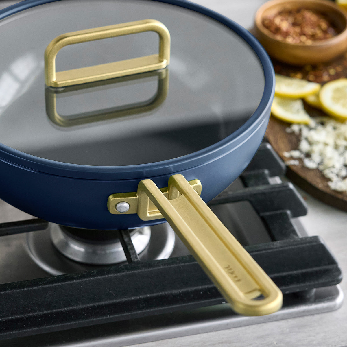 Stanley Tucci 3.25-quart ceramic nonstick Piccolo pan in Marino Blue with a glass lid and gold-toned handles on a stovetop.