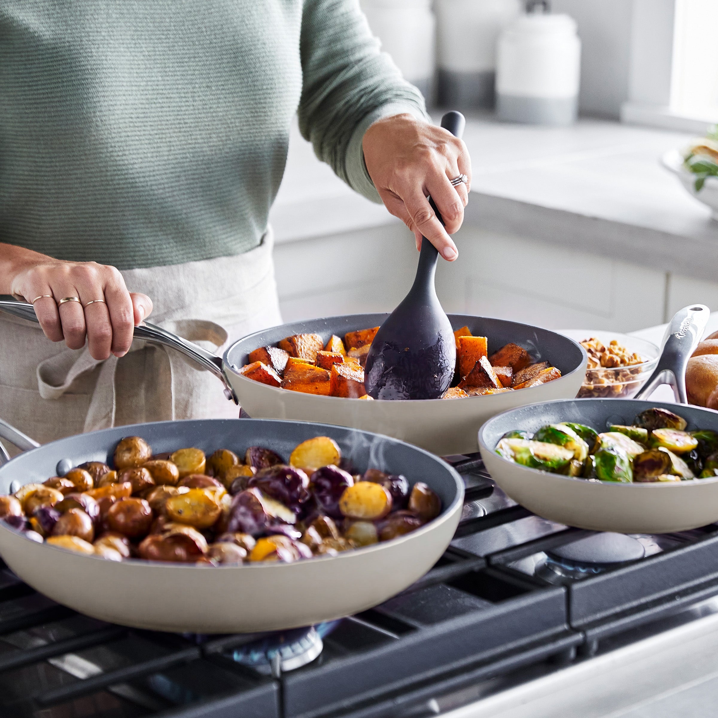 Valencia Pro ceramic nonstick frypan set in three sizes with potatoes, squash, and Brussels sprouts cooking on a stovetop.