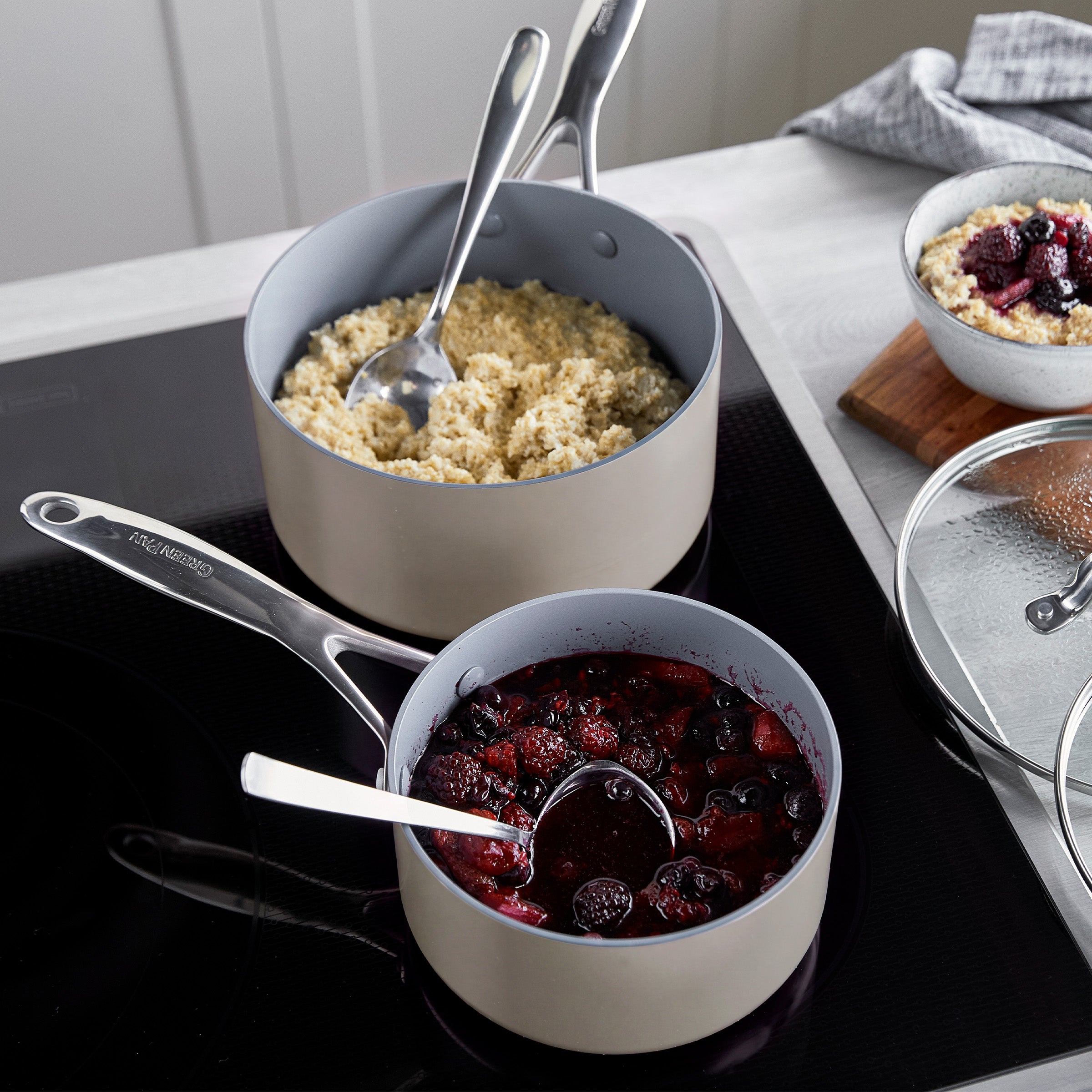 Two taupe ceramic saucepans with lids and spoons on a stovetop, shown as a 1.5-qt and 3-qt set.