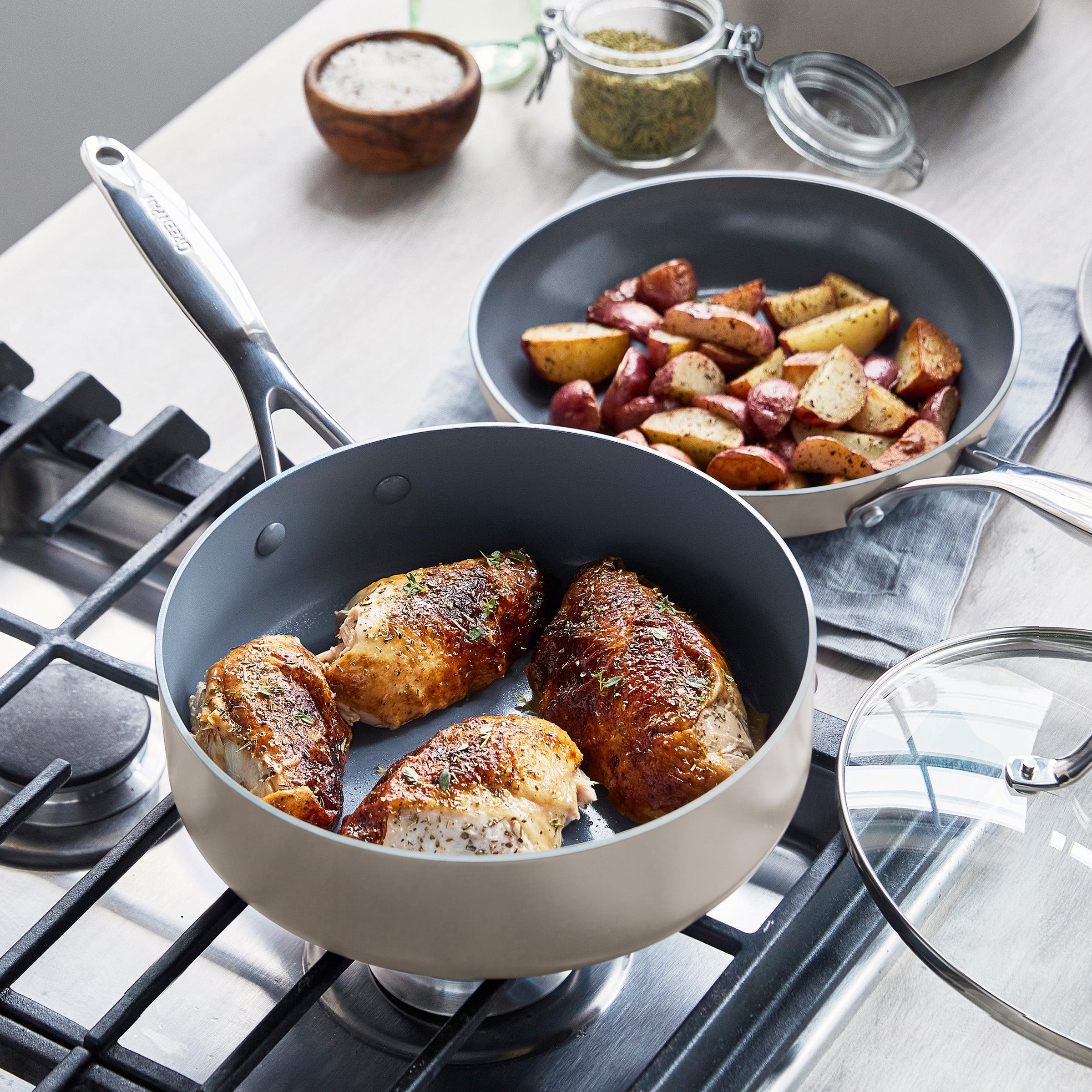 Chicken breasts cook in a gray ceramic nonstick skillet next to roasted potatoes.