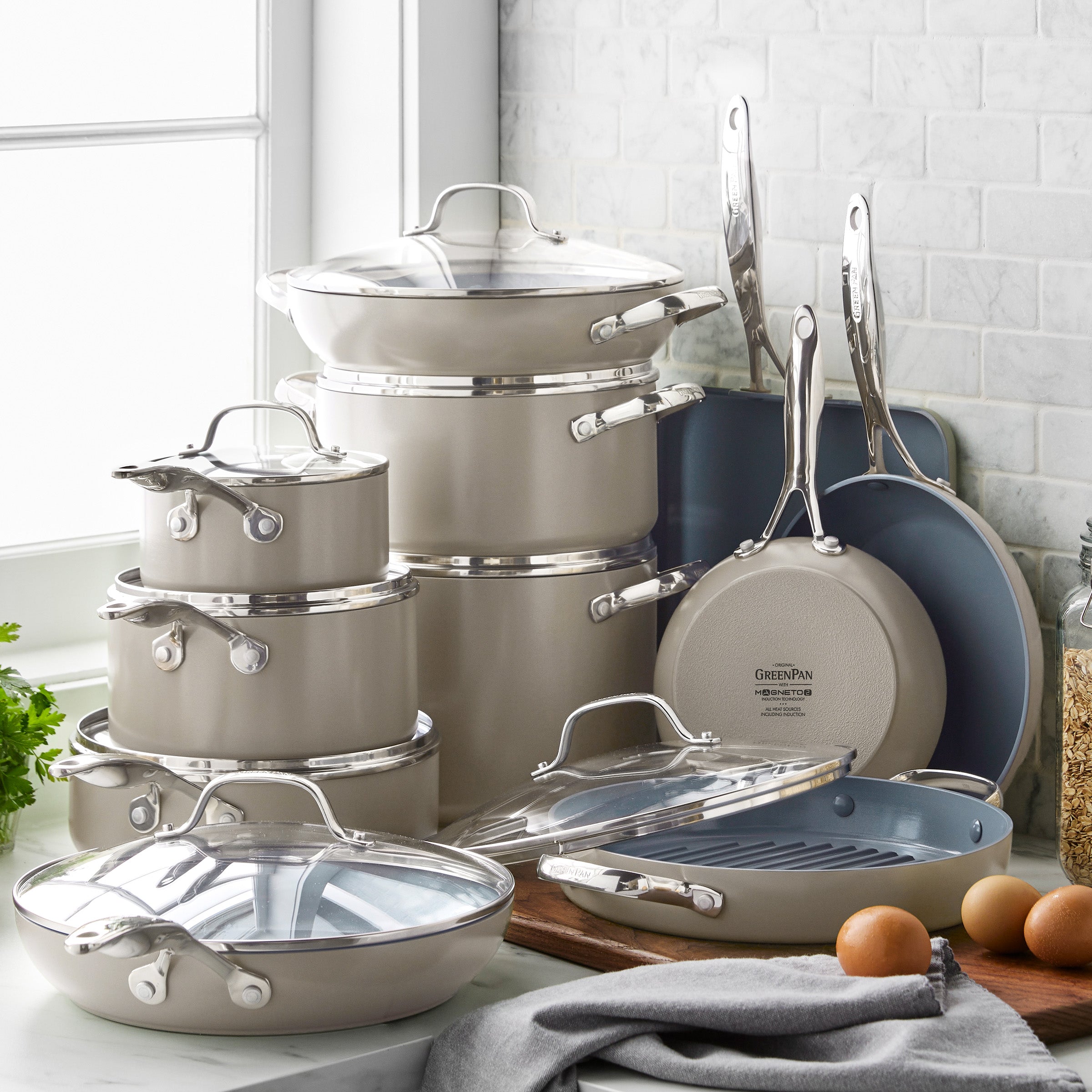 Taupe ceramic 19-piece cookware set on a kitchen counter with eggs and herbs nearby.