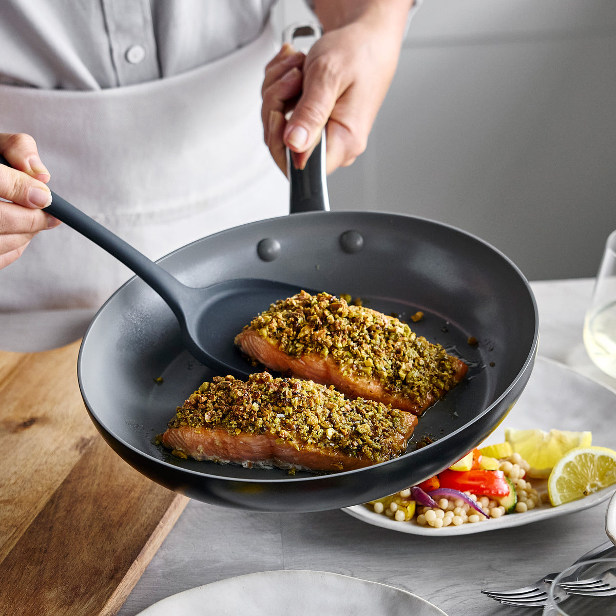 Nut-crusted salmon fillets being lifted with a black spatula from a Chatham Pro Ceramic Nonstick 12-piece cookware skillet.
