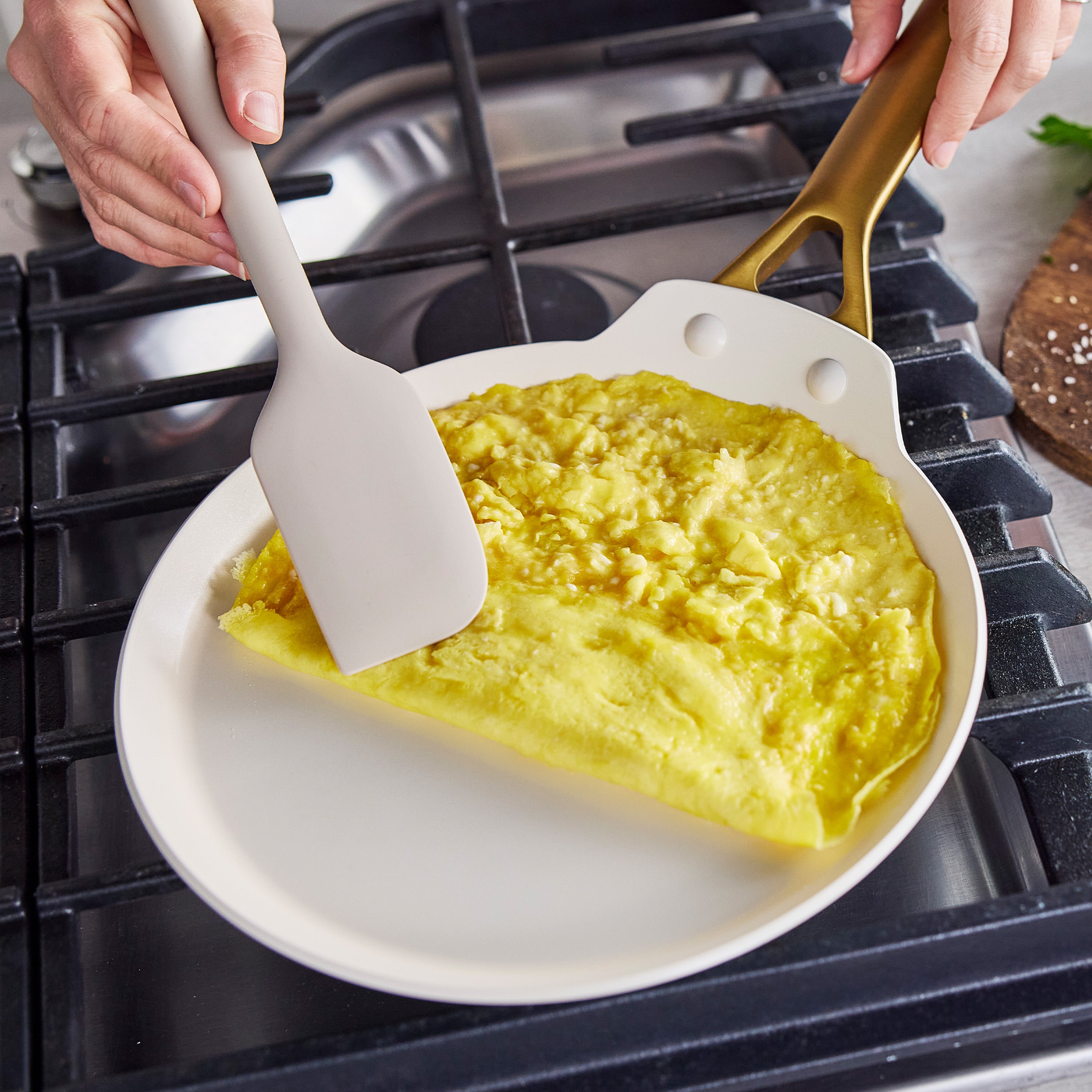 Folding a yellow omelette with a white spatula in a light-colored Reserve Pro Ceramic Nonstick 10″ crepe pan on a stove.