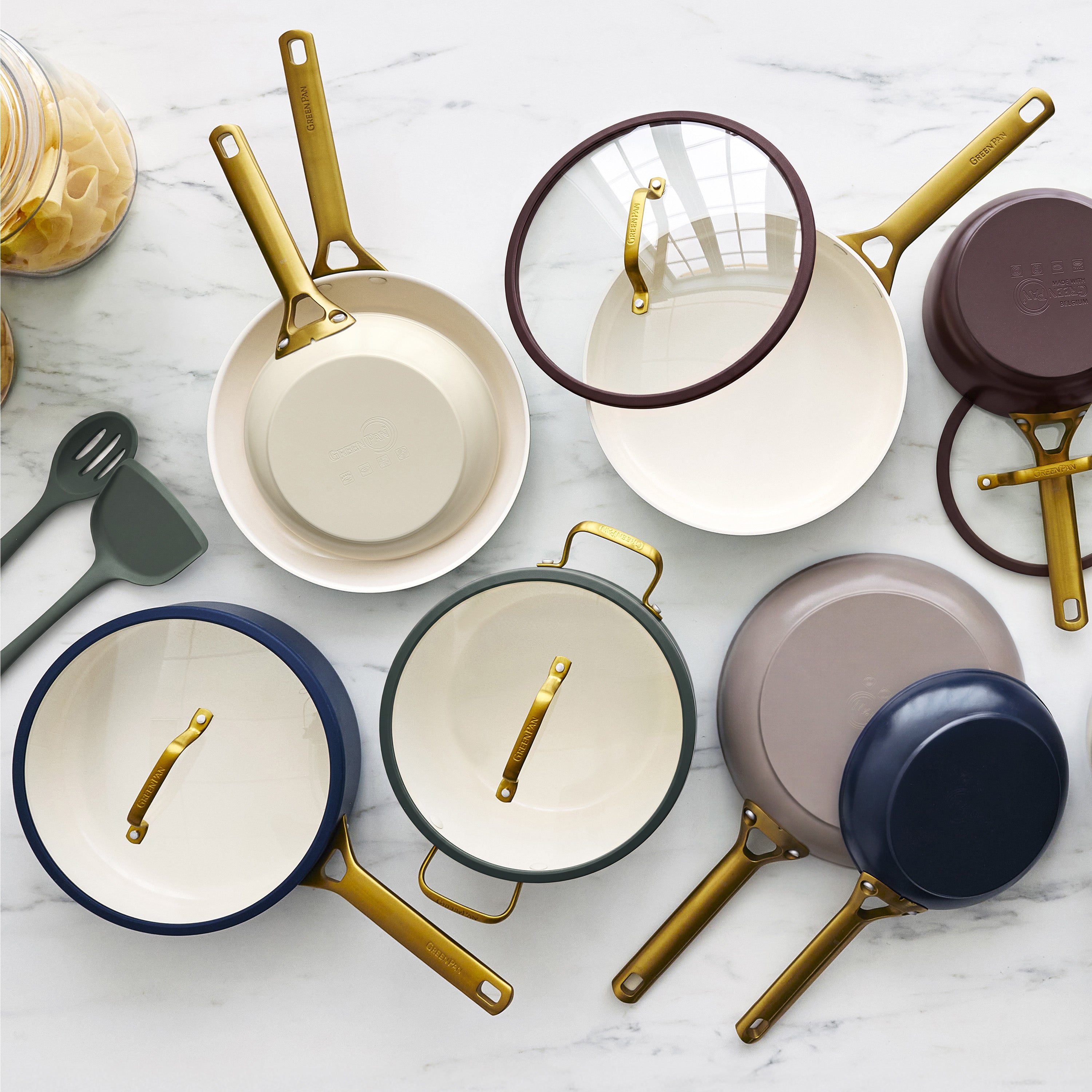Latte-colored 10-piece ceramic cookware set with gold handles on marble counter, near utensils and a pasta jar.