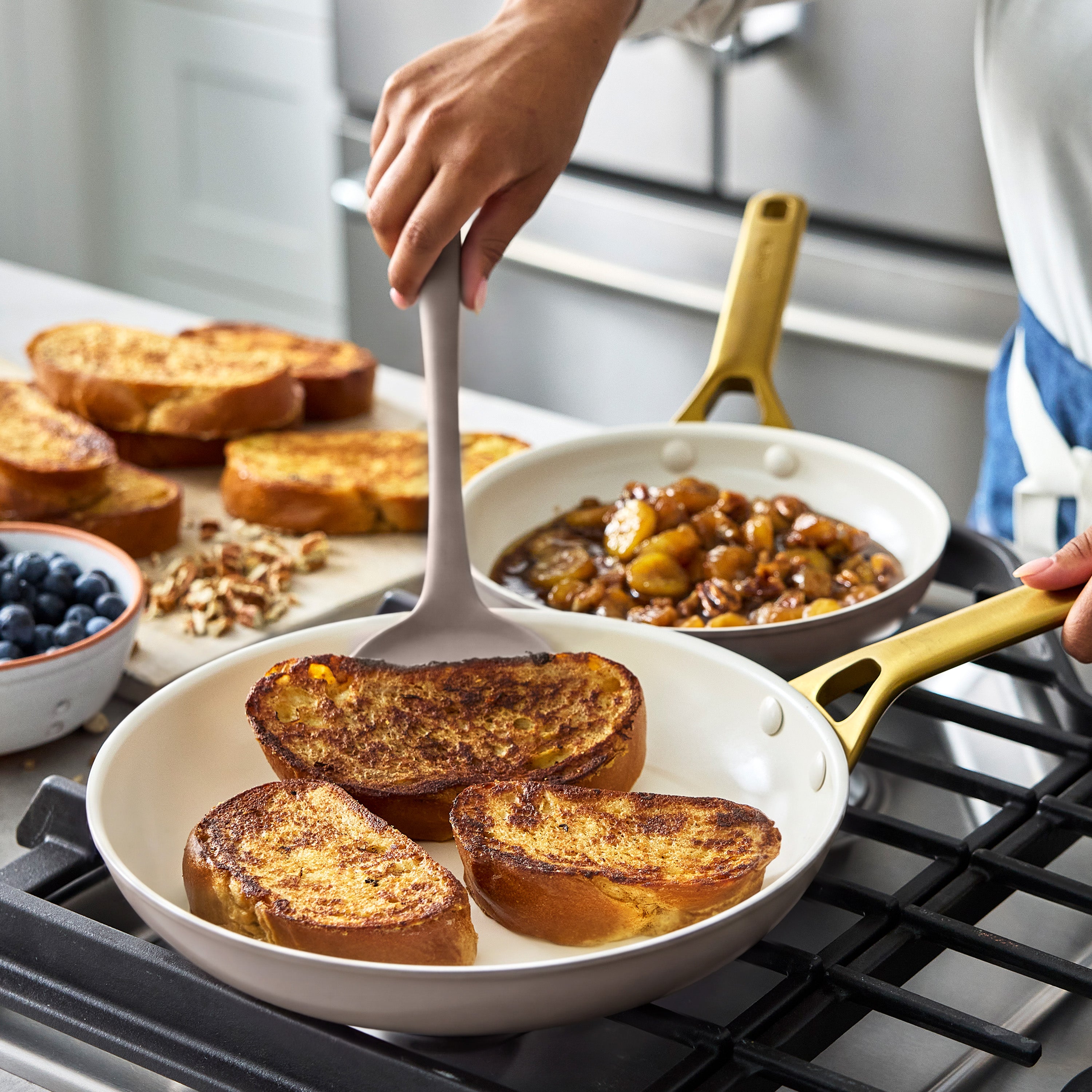 French toast and caramelized bananas cook in a light beige ceramic nonstick pan on a stove.